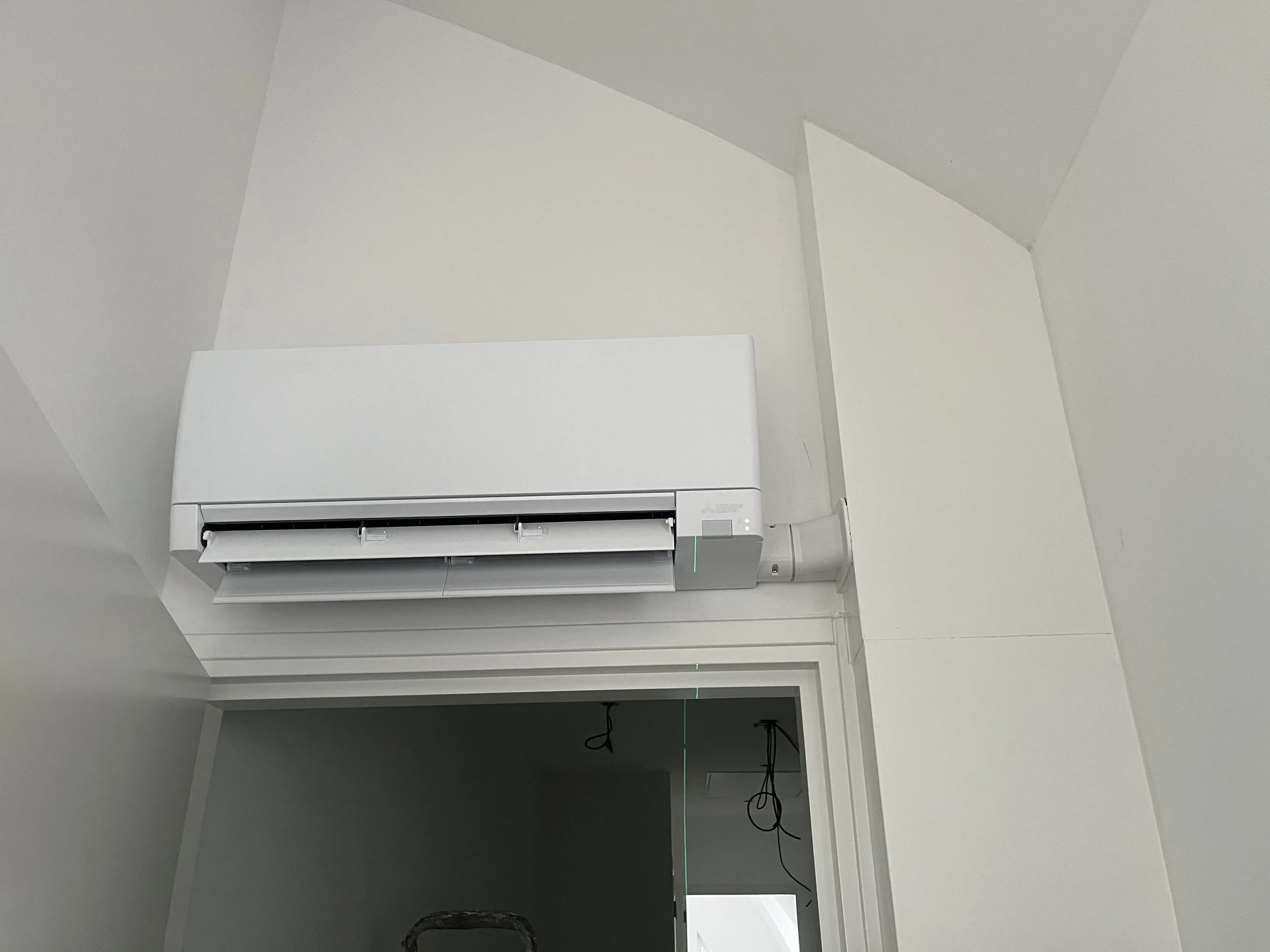 Witte wandairconditioning unit bevestigd aan een witte muur, boven een deuropening
