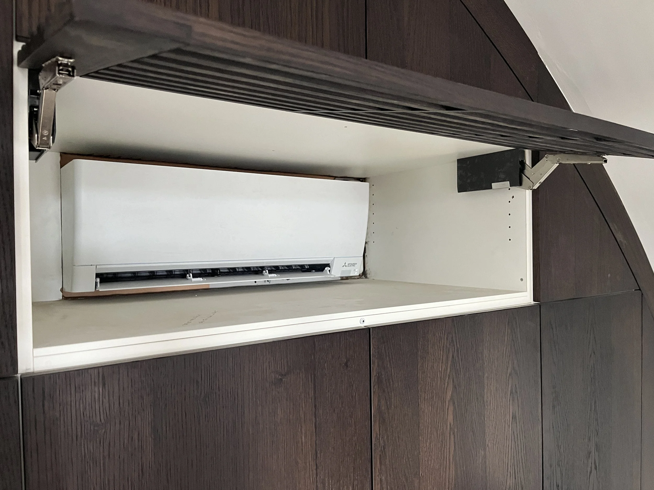 De afbeelding toont een geïnstalleerd airconditioningunit in een ingebouwde kast, met de frontafdekking verwijderd, waardoor de binnenkant zichtbaar is.