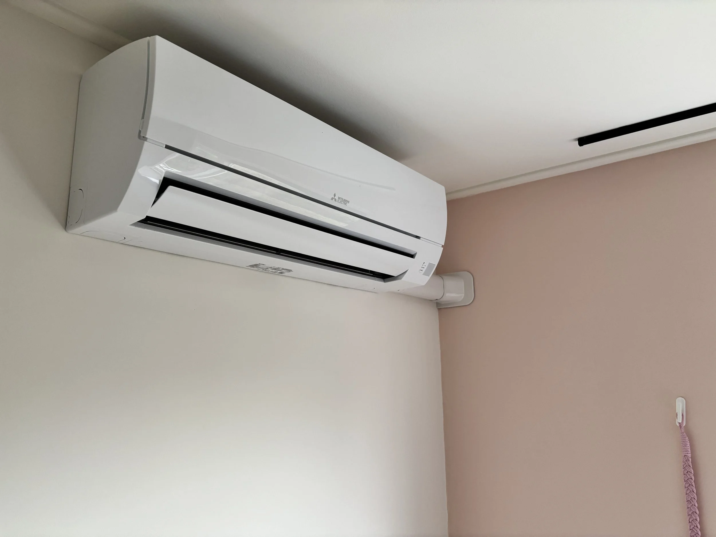 Wit muur en een Split airconditioning unit bevestigd aan de muur, naast een plafond met een plafondrooster en een roze muur met een plafondtelefoon en een pink-lijn.