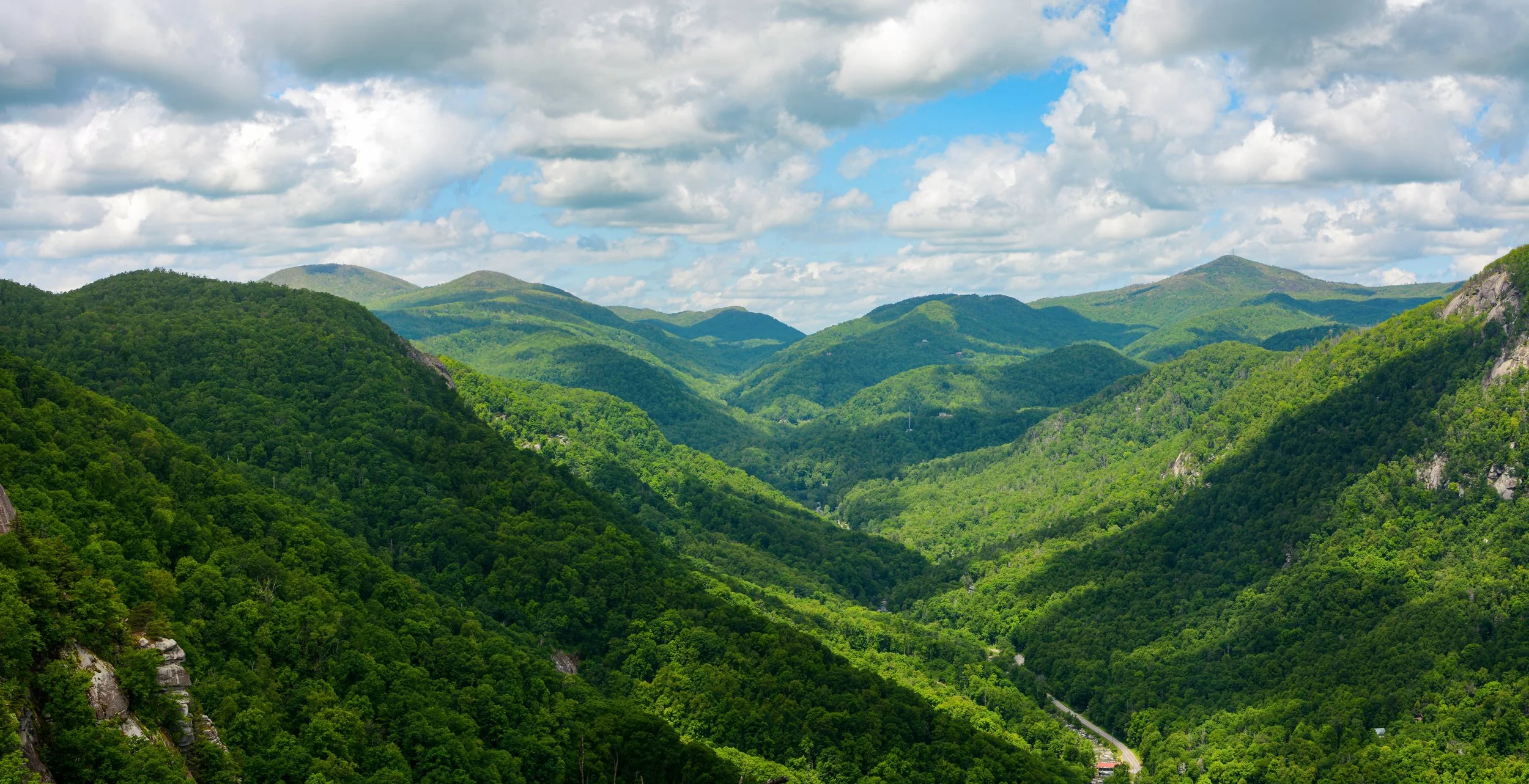 Green mountain range with lush forested hills under a partly cloudy blue sky