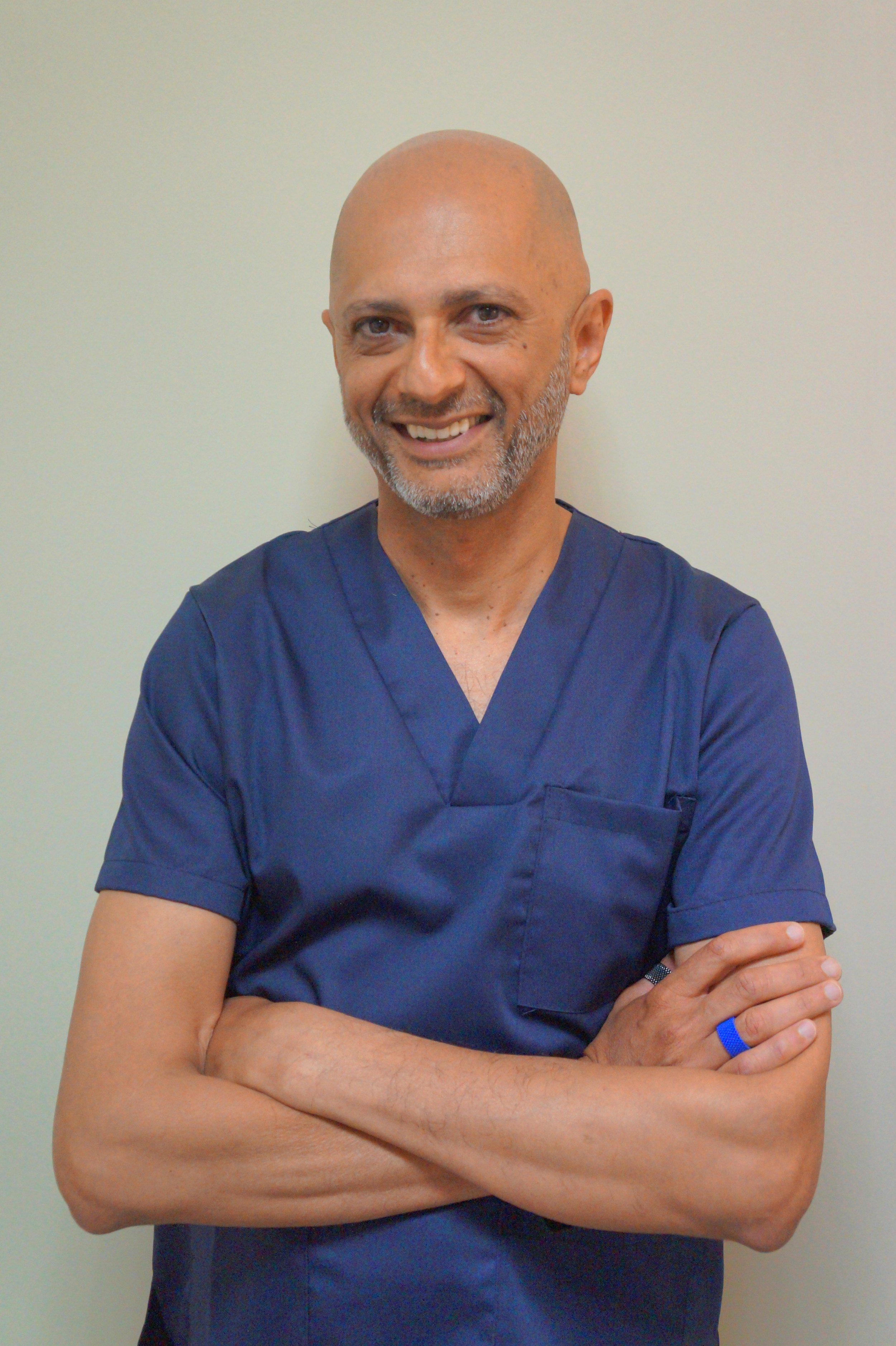 Altaf, profissional de saúde, com os braços cruzados, com parede clara como fundo.