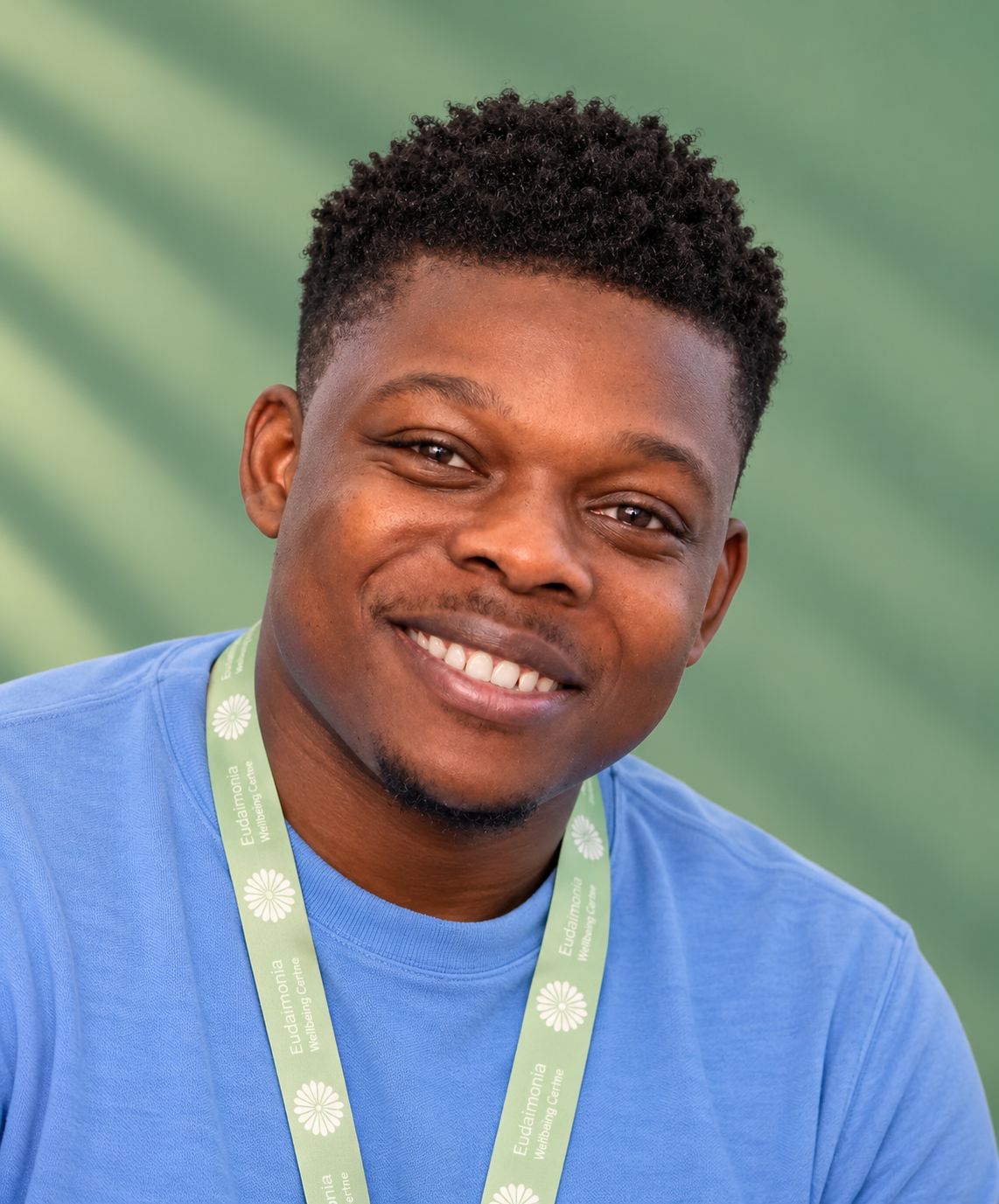 Smiling young man with short black hair, wearing a light blue shirt, outdoors on a sunny day.