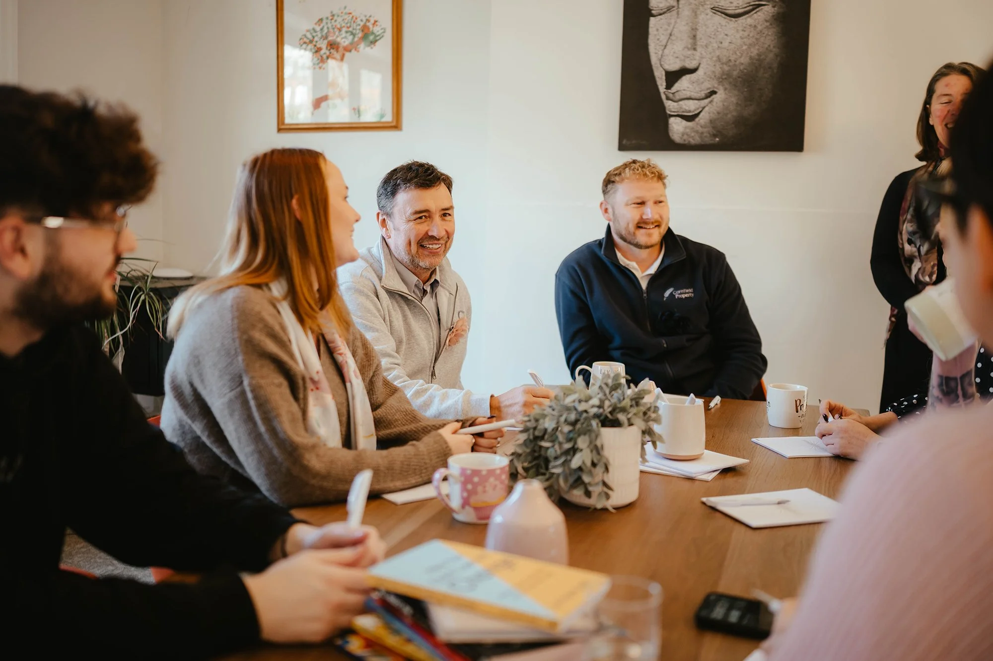 A group of people sitting around a table laughing and talking whilst taking part in a workplace wellbeing exercise.