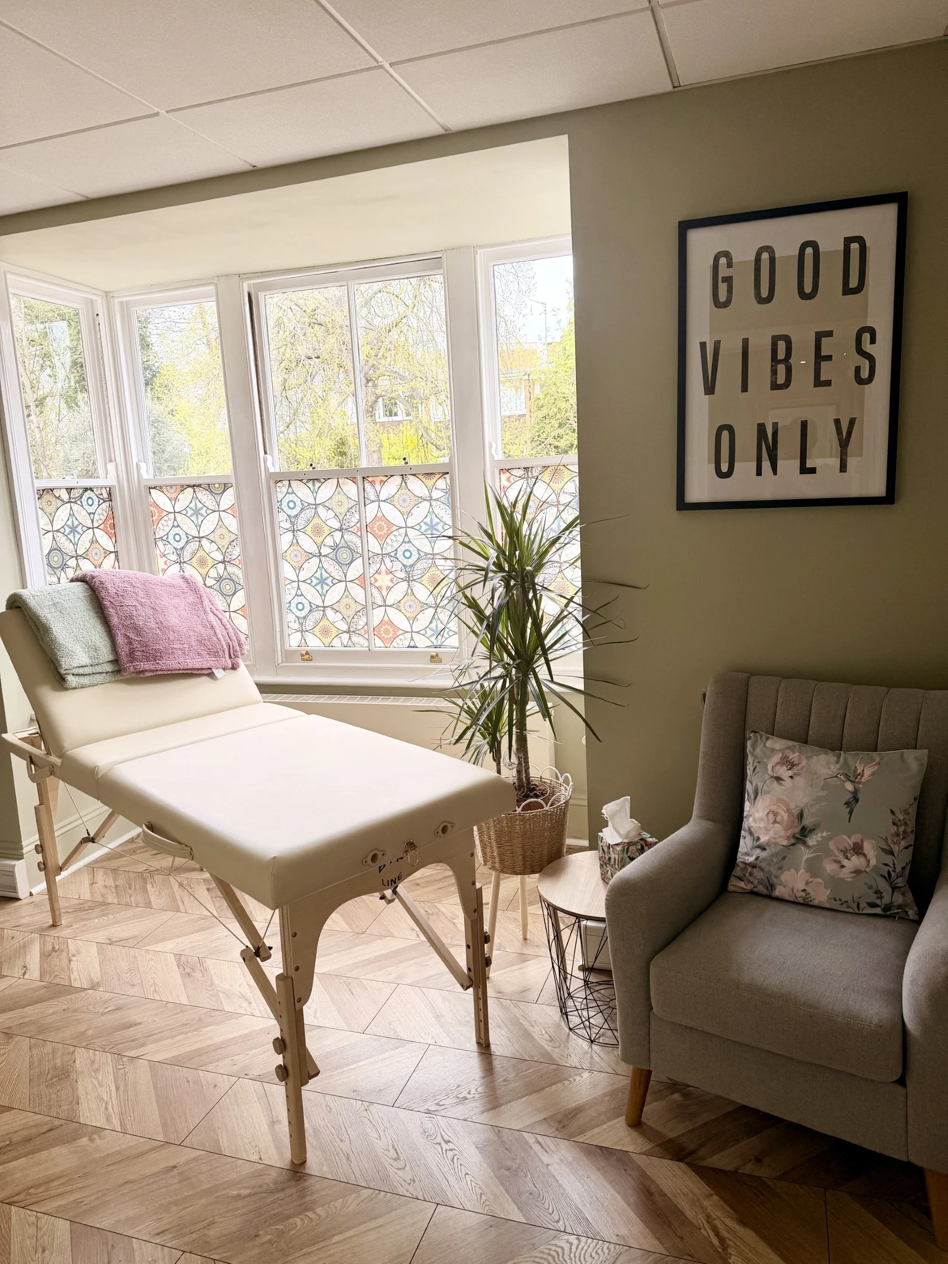 Warm and bright clinical therapy space with a treatment bed, two blankets and a grey chair in the room.