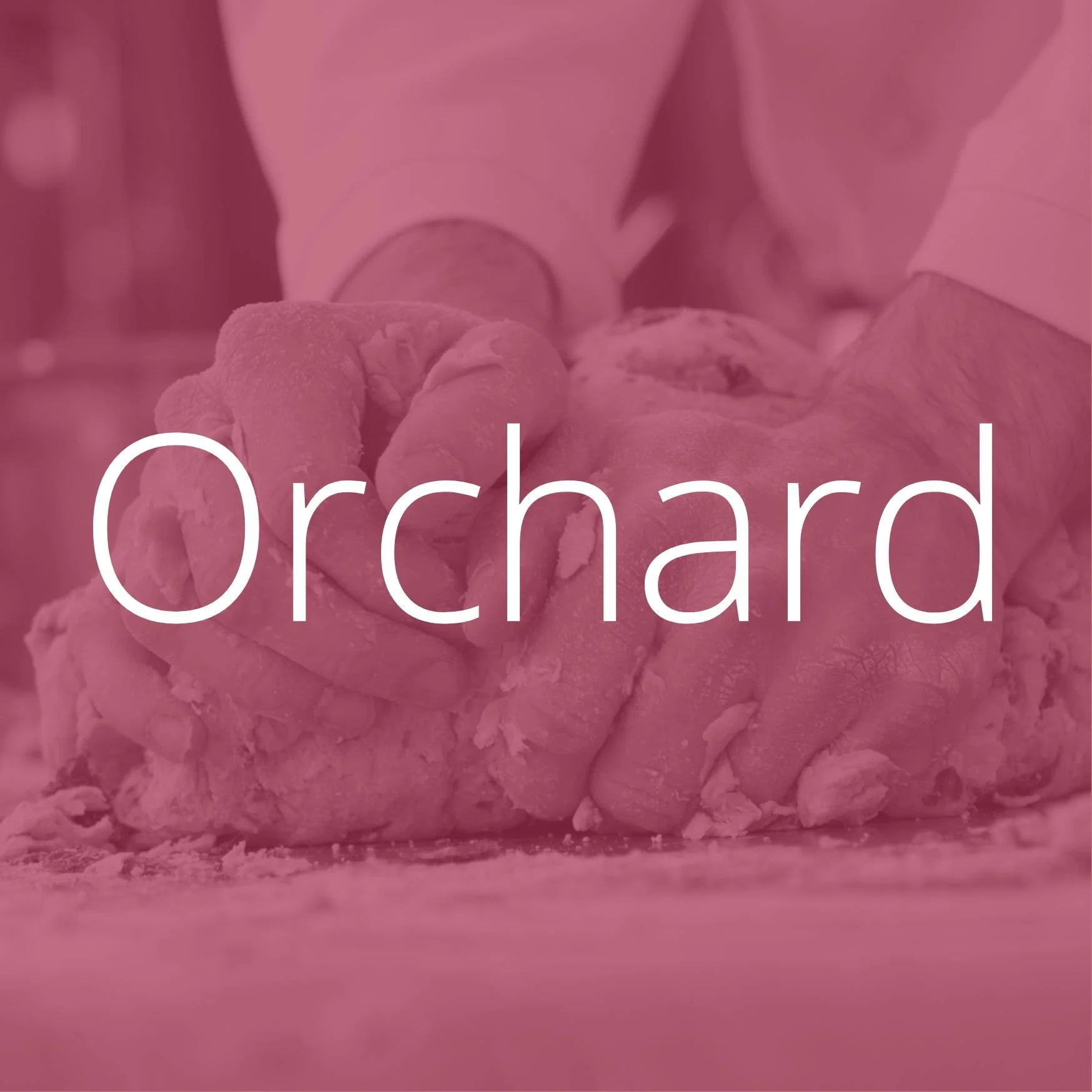 A smiling woman with dark curly hair, wearing glasses with round lenses, hoop earrings, and layered necklaces, sitting indoors with a blurred background.