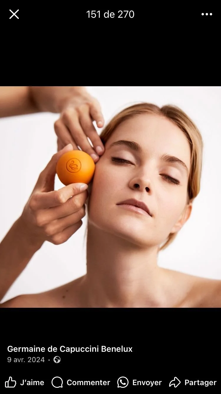 Une femme reçoit un soin du visage avec une balle orange portant un logo de bain croisé, lors d'une séance de massage ou de soin esthétique.