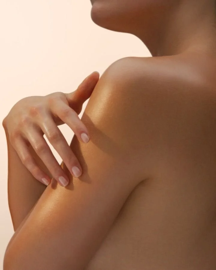 Une personne nue avec une main posée sur l'épaule, montrant la peau et les contours du corps dans un éclairage doux.