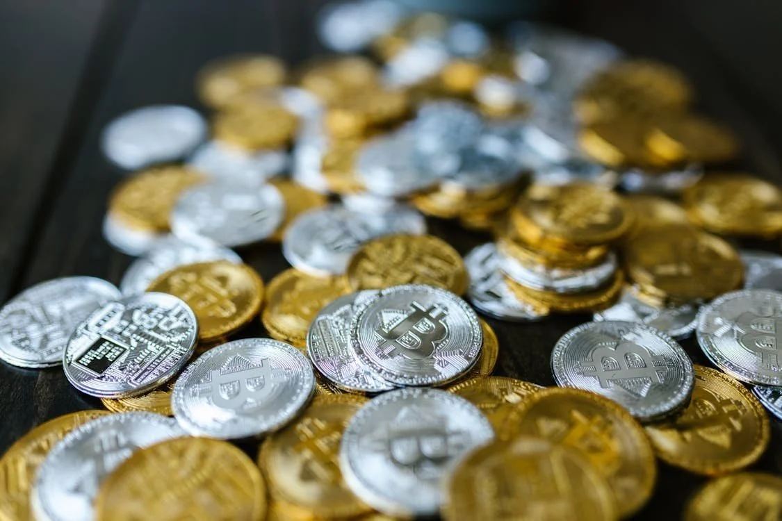 A collection of silver and gold Bitcoin coins scattered on a dark surface.