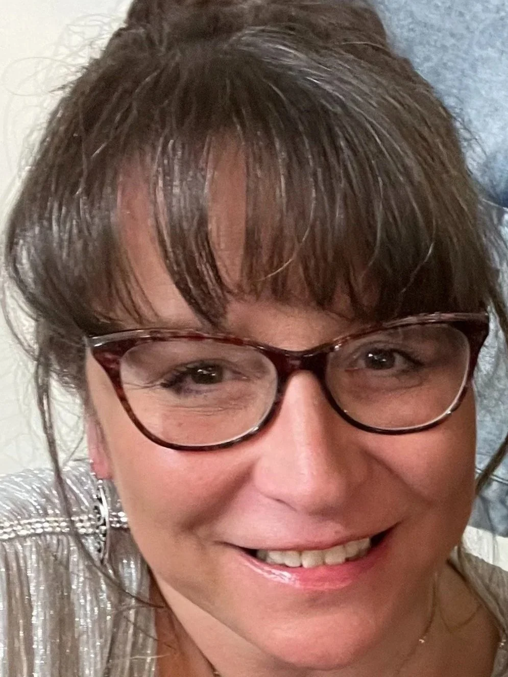 Close-up of a smiling woman with brown hair, glasses, and earrings.