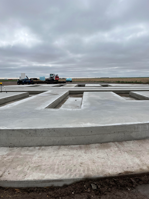 Construction site with concrete foundation, construction equipment, and a cloudy sky.