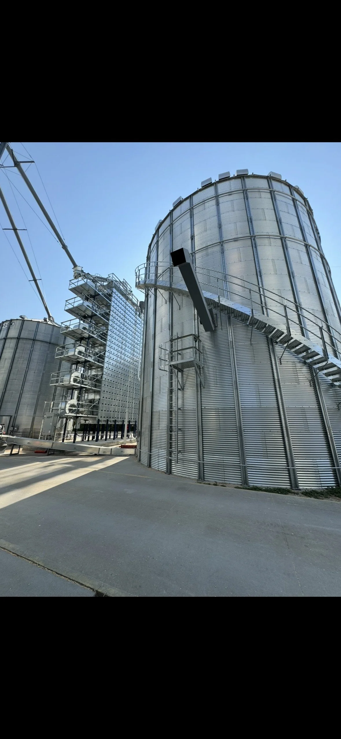 Large industrial grain silos with metal ladders and staircases against blue sky.