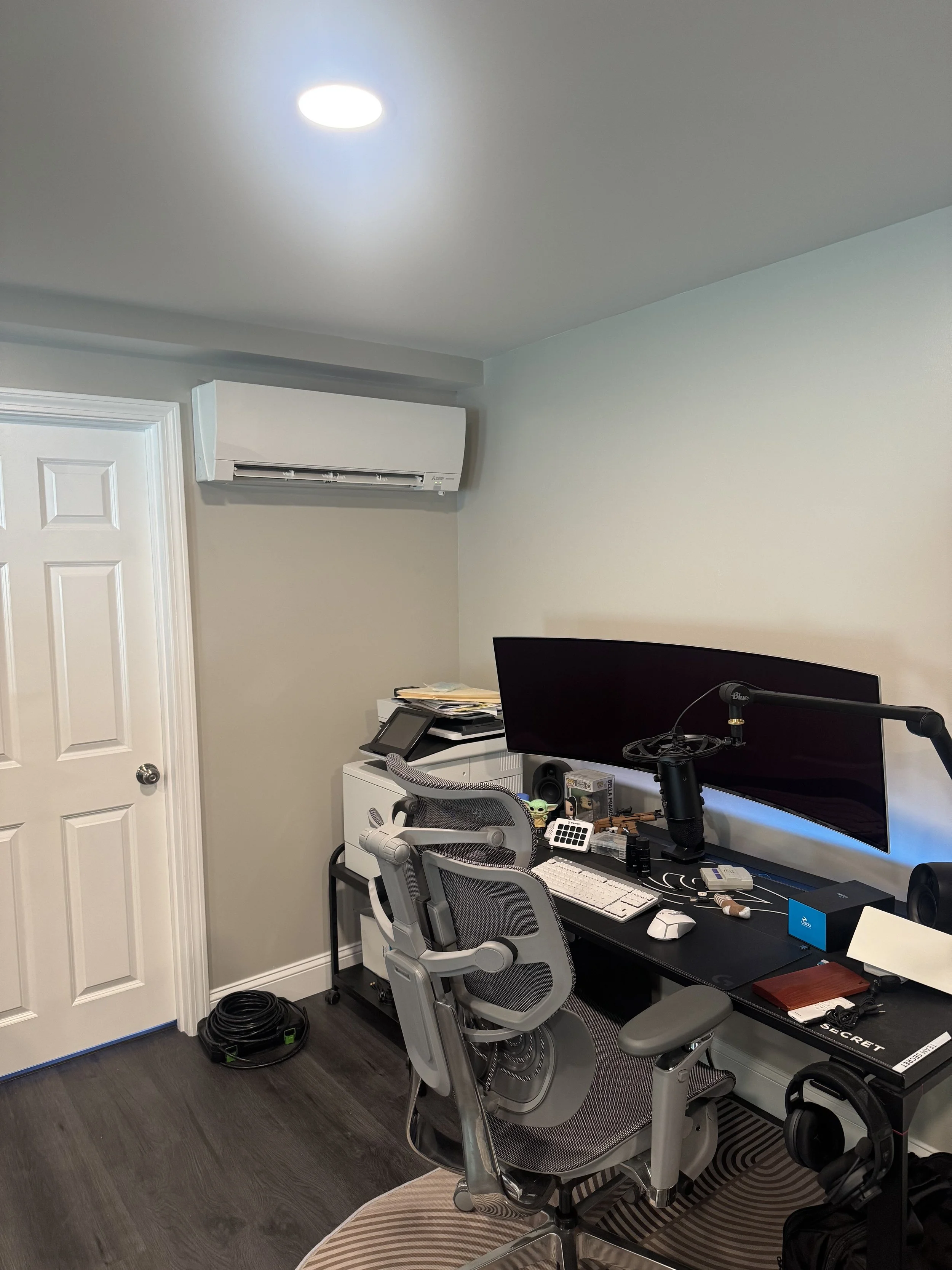 Home office with desk, two monitors, ergonomic chair, and various office supplies, next to a white dresser and wall-mounted air conditioner.