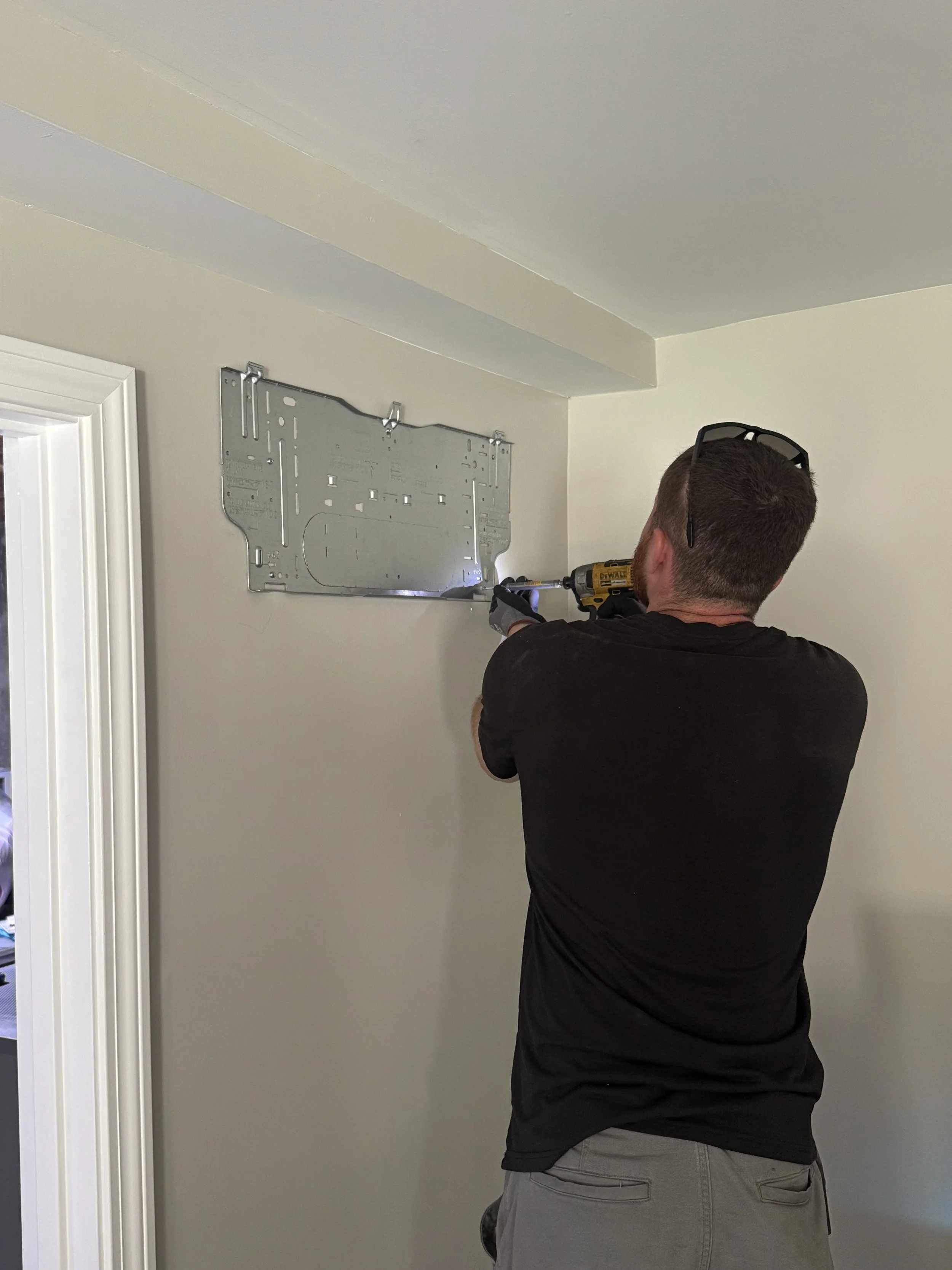 A man installing a metal bracket on a white wall using a cordless drill.