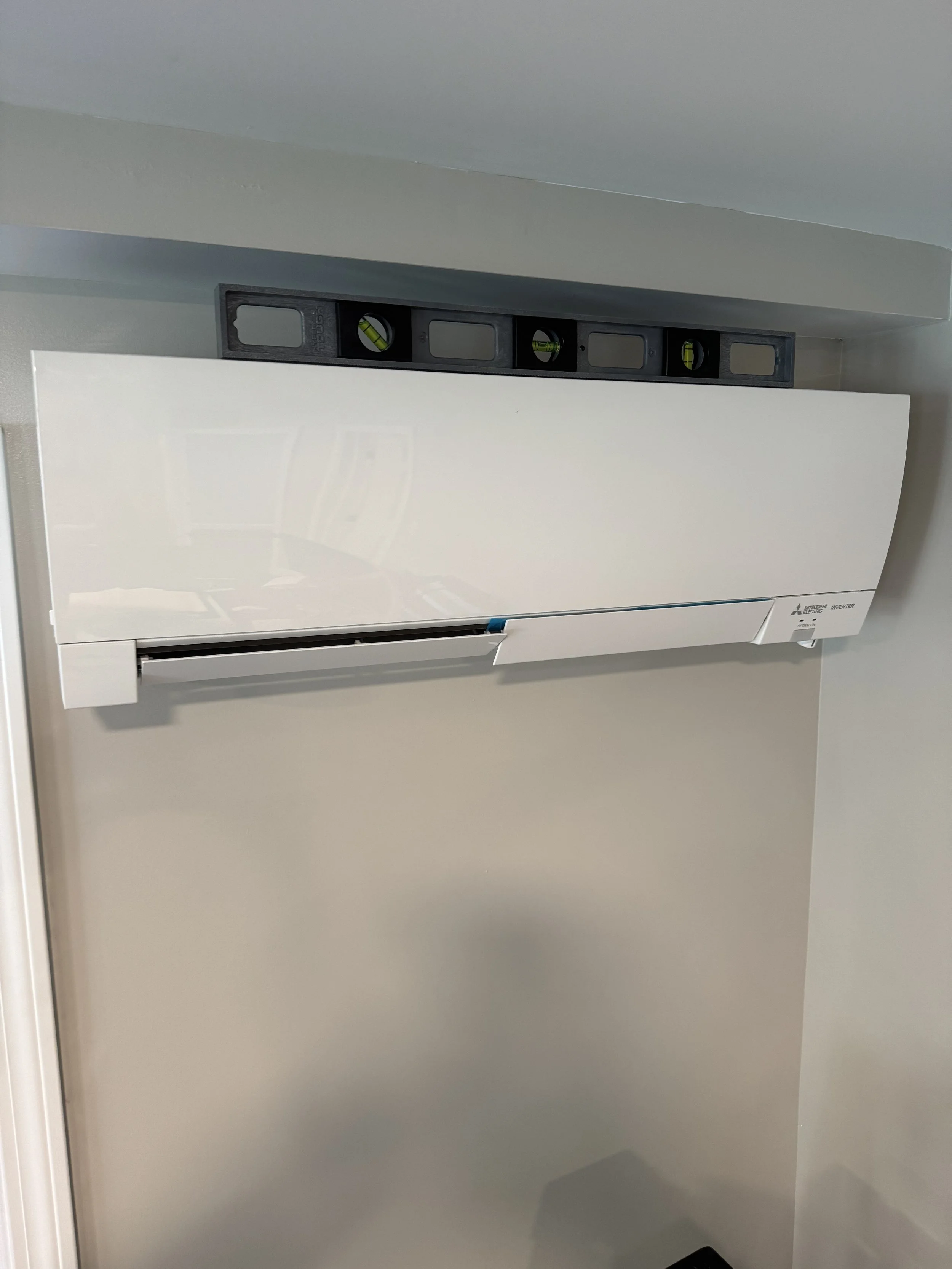 White Mitsubishi air conditioning unit mounted on the wall under a black level tool.