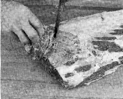 Close-up of a hand using a paintbrush to paint a wooden surface.