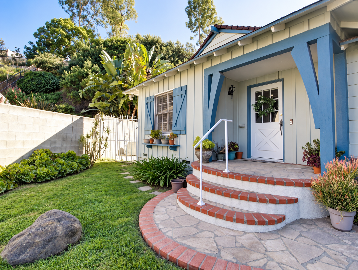 Exterior of front of house, blue shutters and white facade with red brick steps leading to house