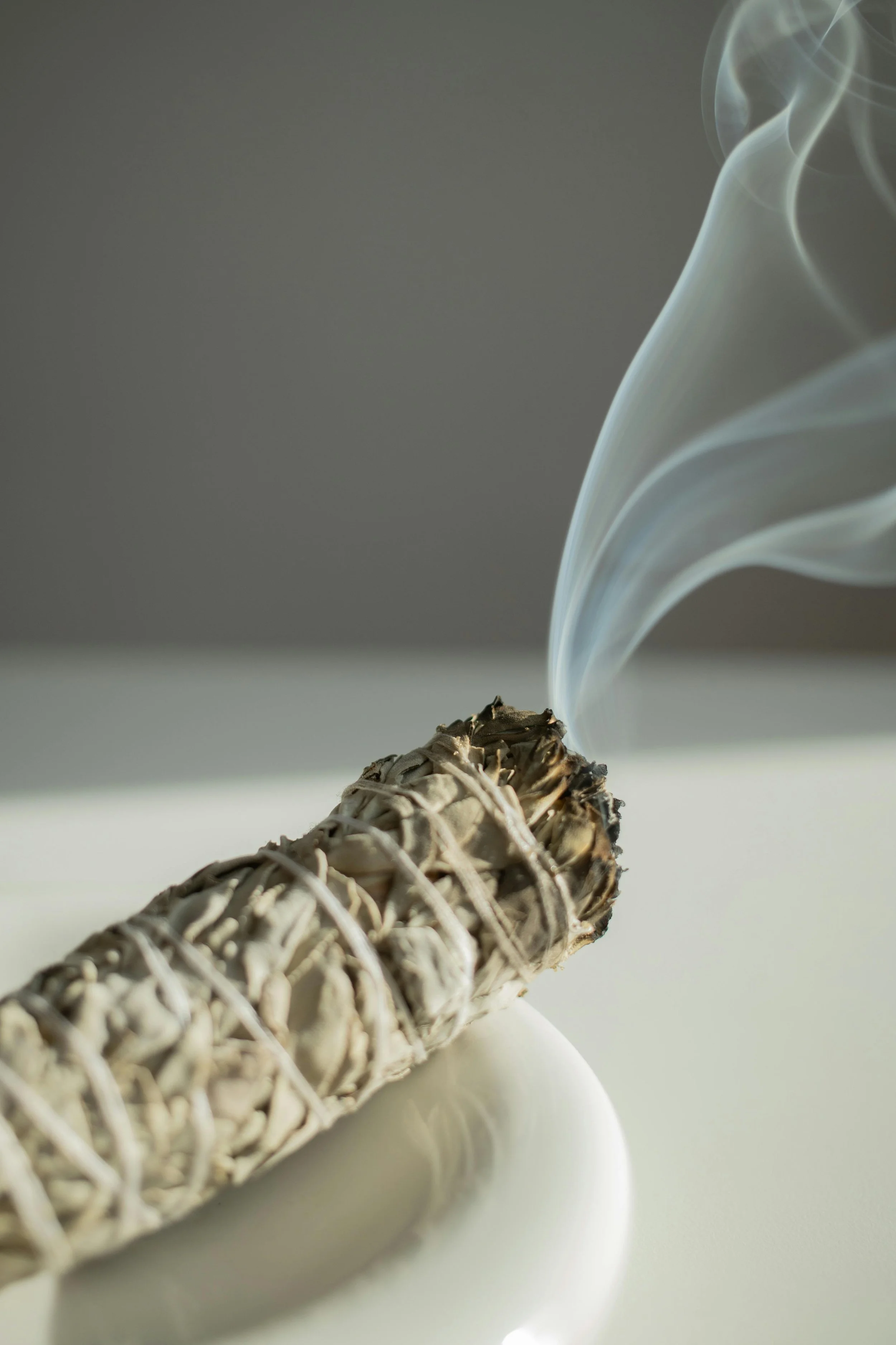 A smoldering sage bundle with smoke rising from it, placed on a white dish.