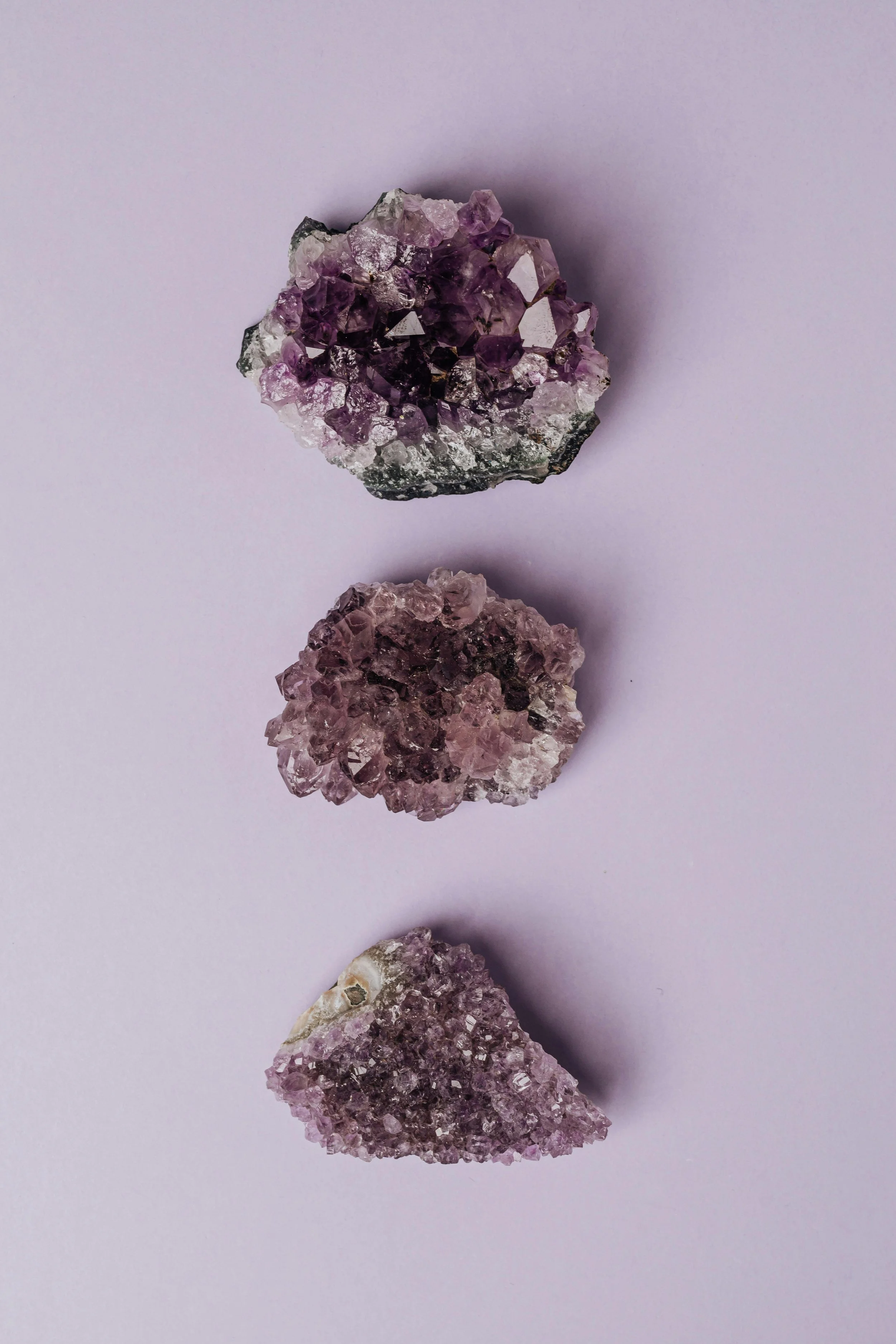 Three amethyst crystals arranged vertically on a light pink background.