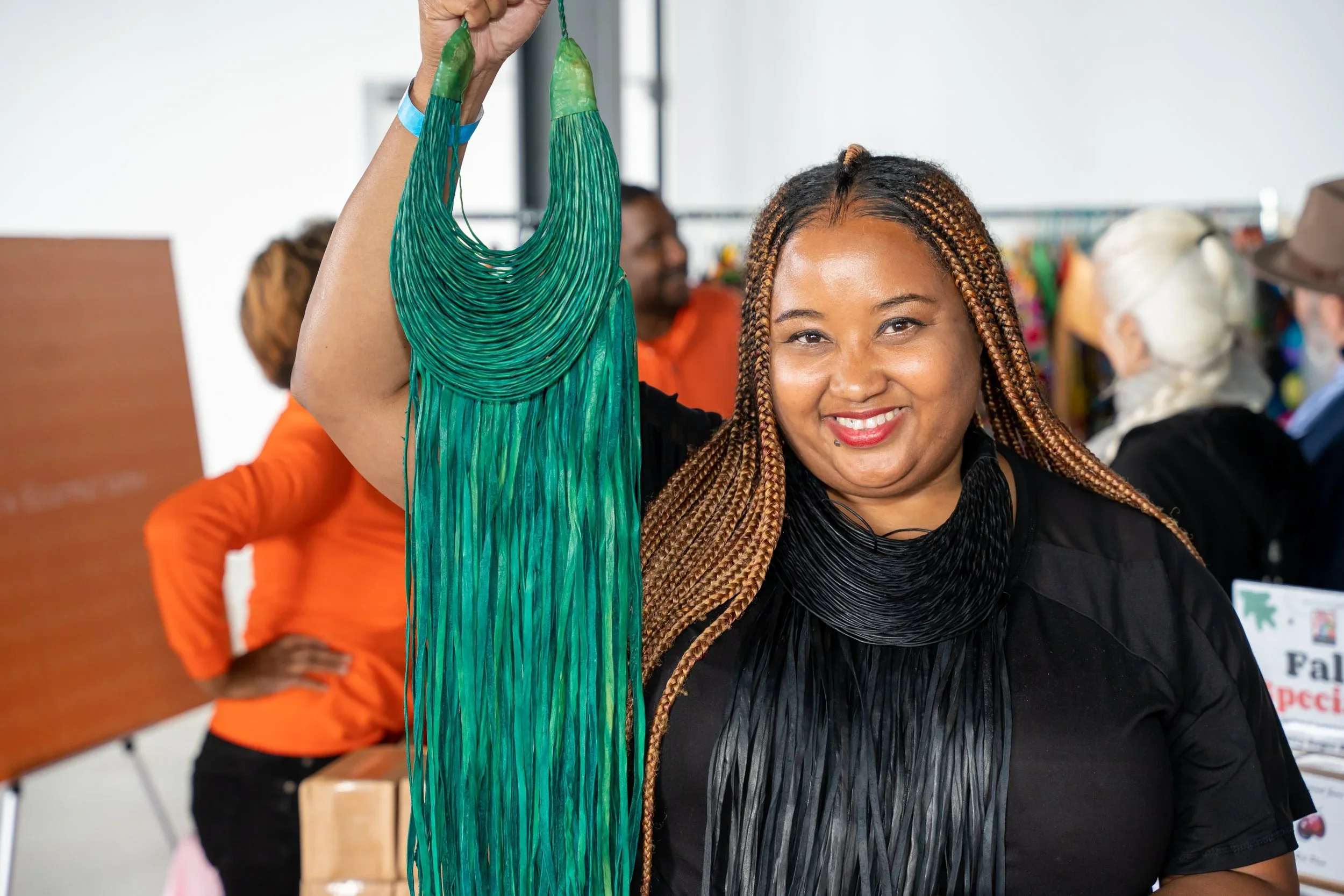 Woman in black top with long braided hair holding up a green craft item