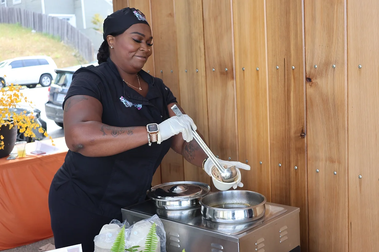 Woman dressed in black, wearing white gloves serving soup