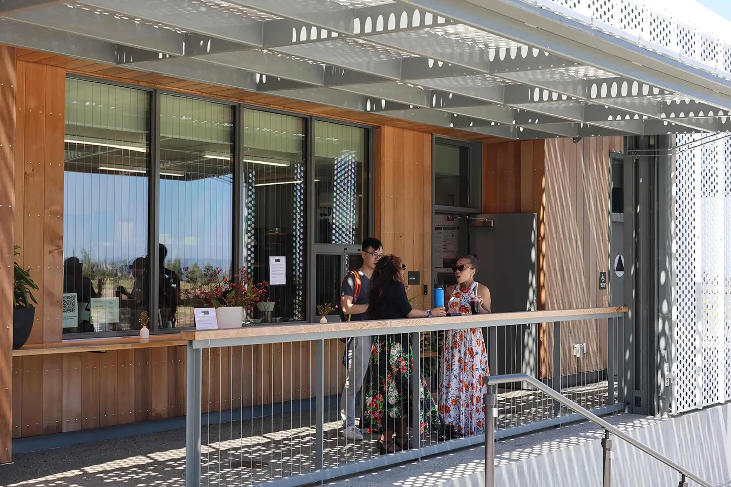3 people in conversation by railing with windows and open door in background
