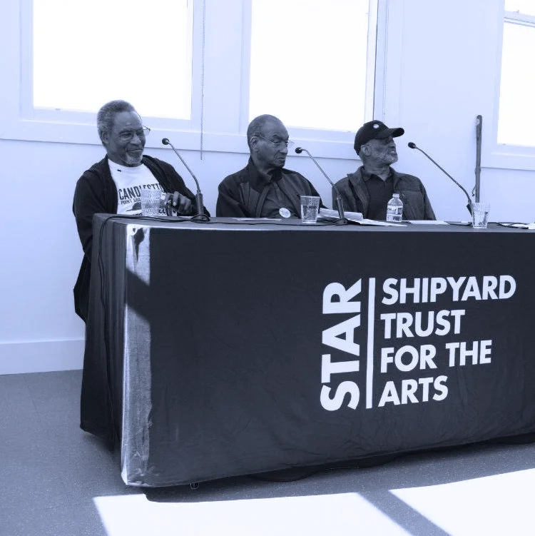 Black and white photo of 3 elderly black men sitting at a table with a tablecloth labeled STAR - Shipyard Trust For The Arts