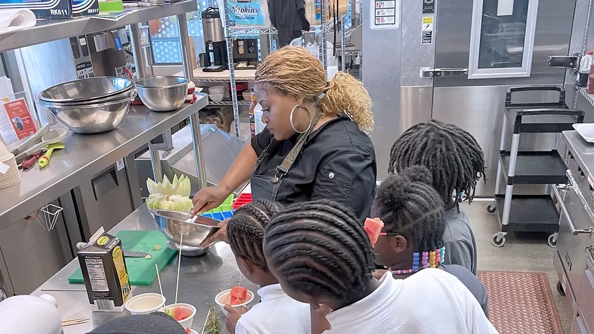 Chef with mixing bowl and 4 children looking on with backs to camera
