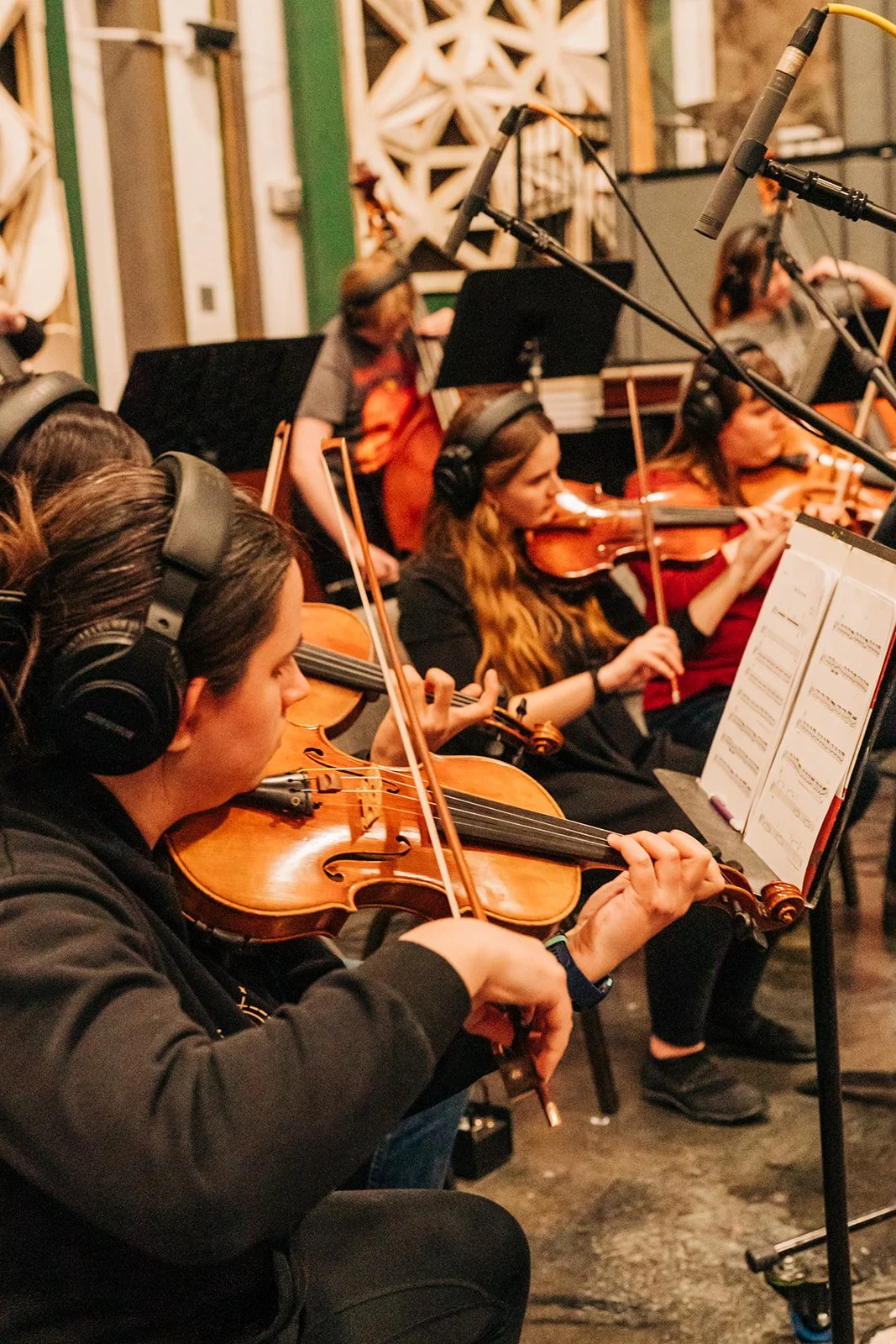 Group of women playing violins in a recording studio with music sheets, wearing headphones.