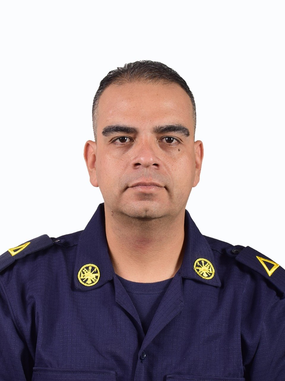 Retrato de un hombre con uniforme policial azul, de piel clara y cabello corto negro, en posición frontal, con fondo blanco.