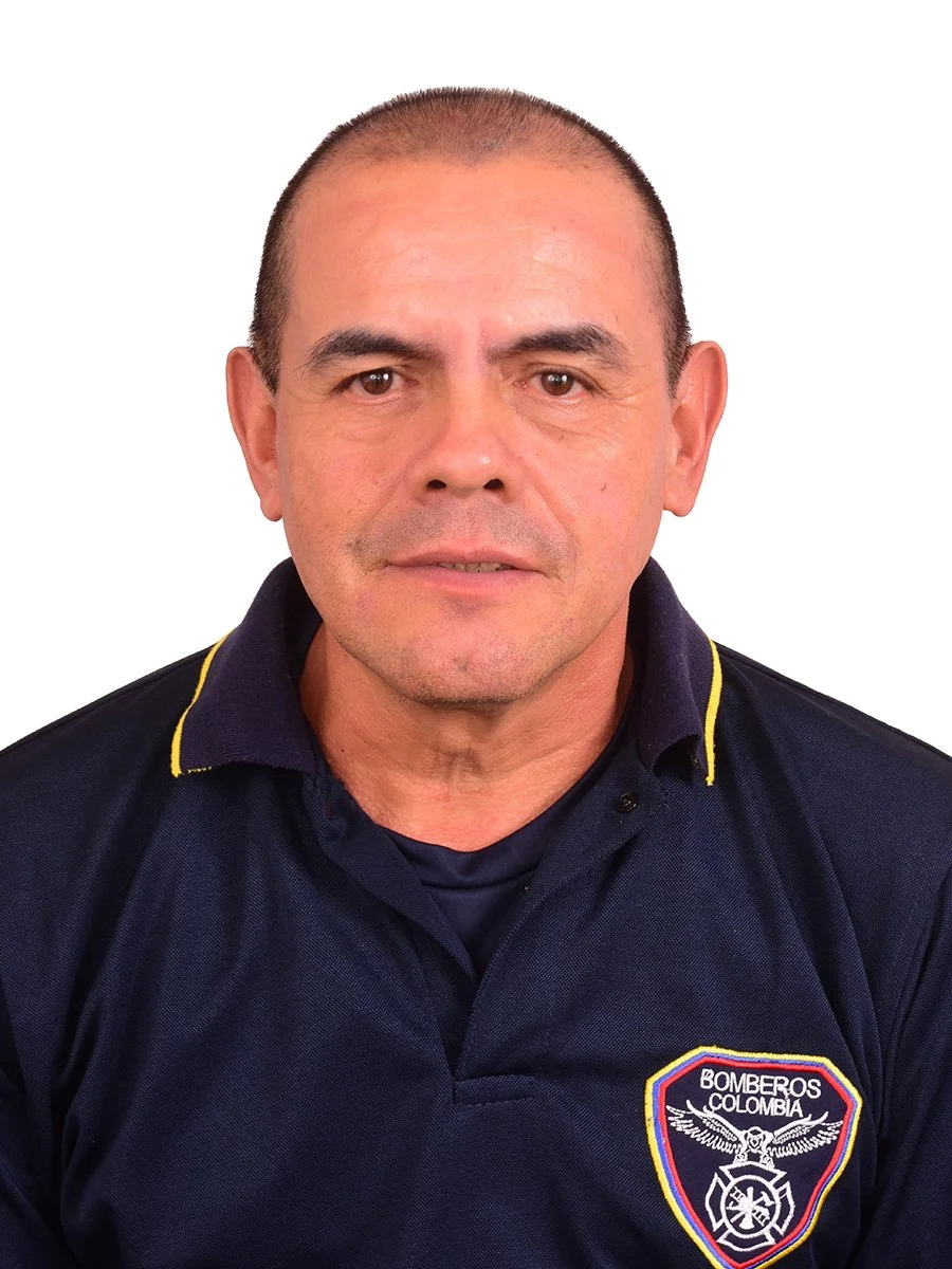 Hombre con cabello rapado, vestido con uniforme de bombero de Colombia, con escudo en el pecho que dice 'Bomberos Colombia' y un símbolo de bombero.
