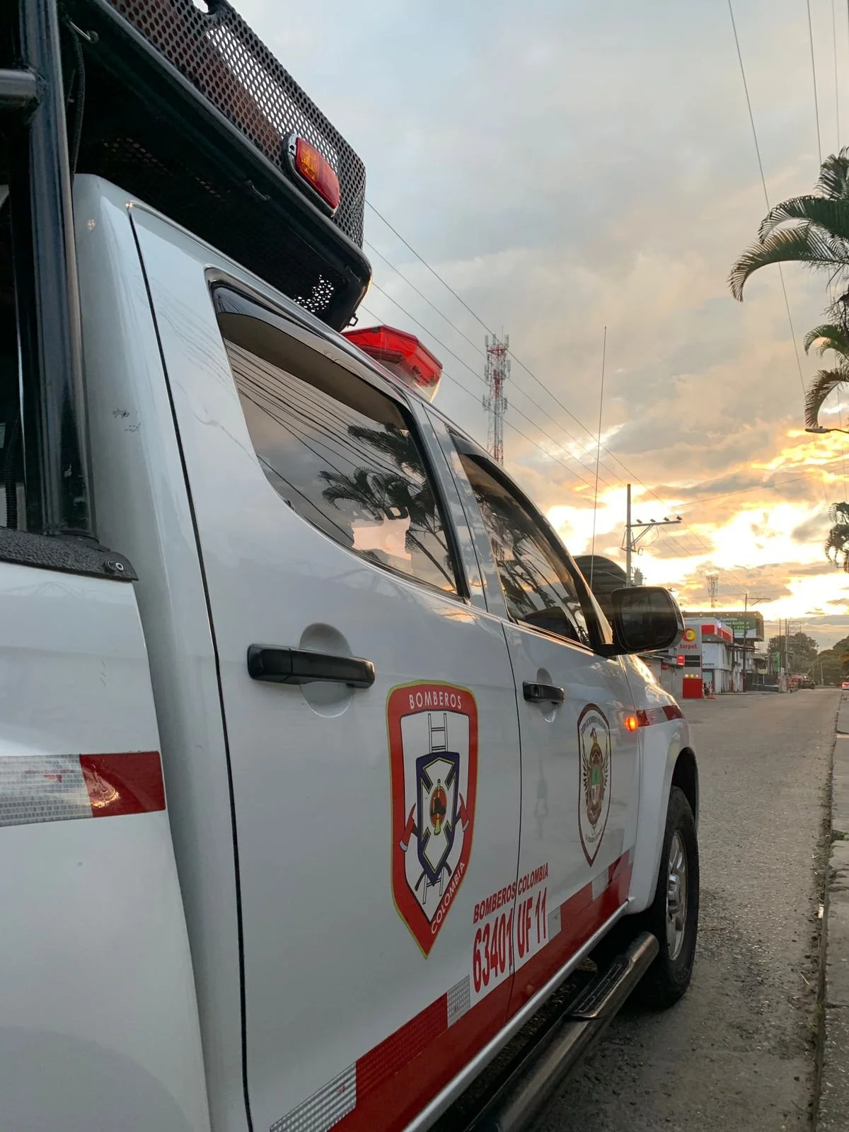 Vehículo de bomberos de Colombia en la calle durante el atardecer, con árbol y cielo nublado en el fondo.