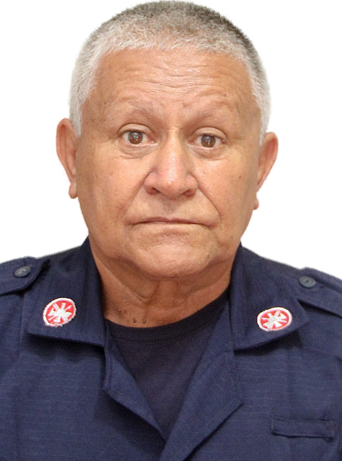 Retrato de un hombre de cabello corto y gris, usando un uniforme de policía con insignias rojas y blancas, fondo blanco.