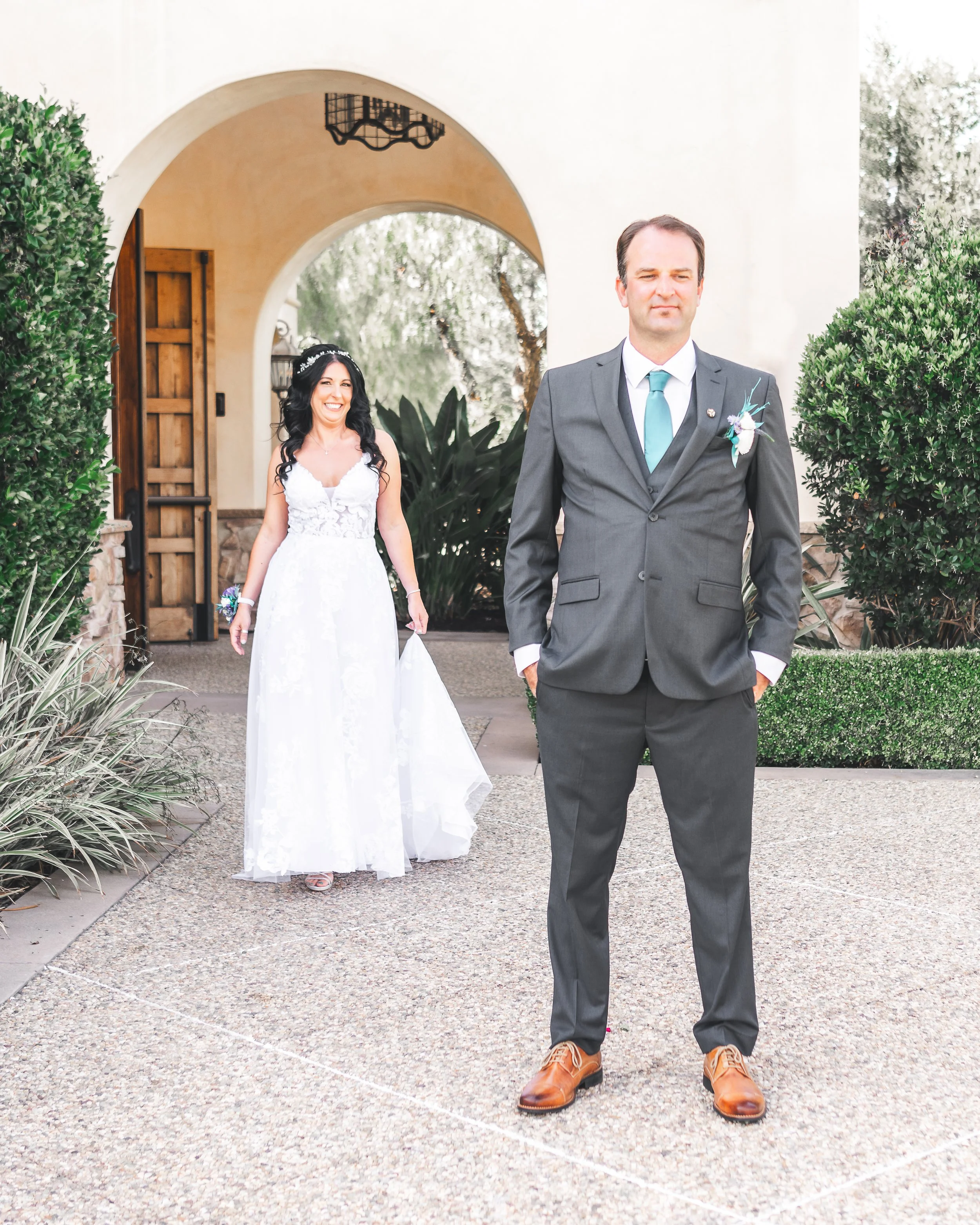 Bride in white gown walks towards groom in suit during first look at wedding.