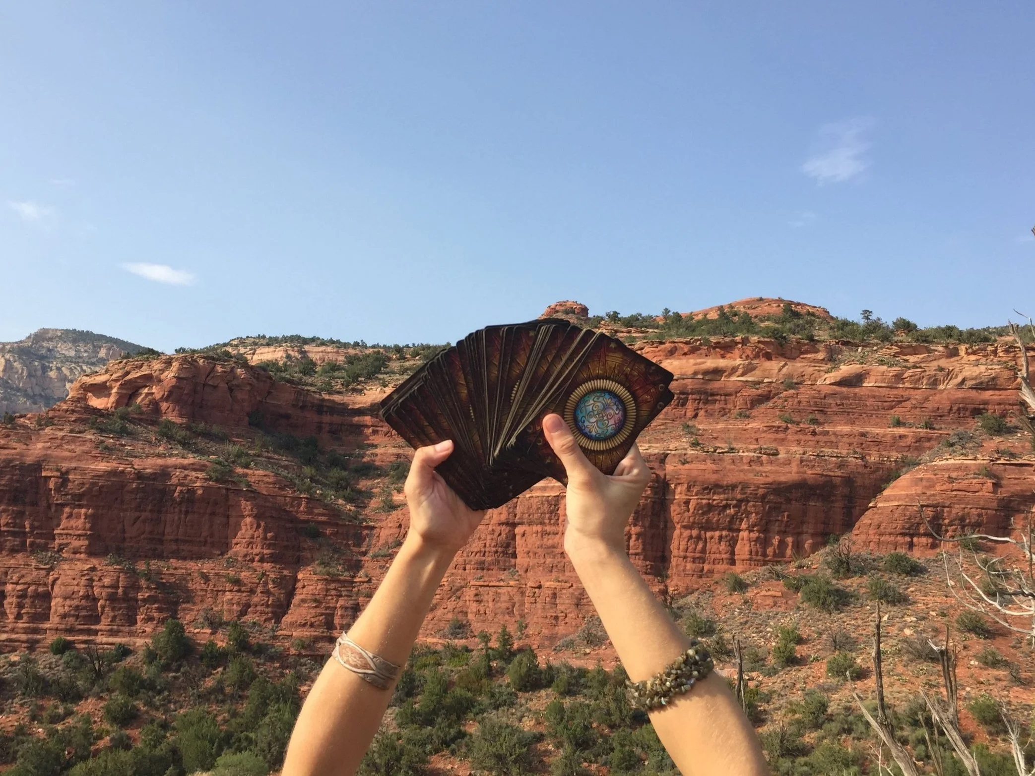 my hands holding up tarot cards in front of the red rocks of Sedona Arizona on a clear blue sky day