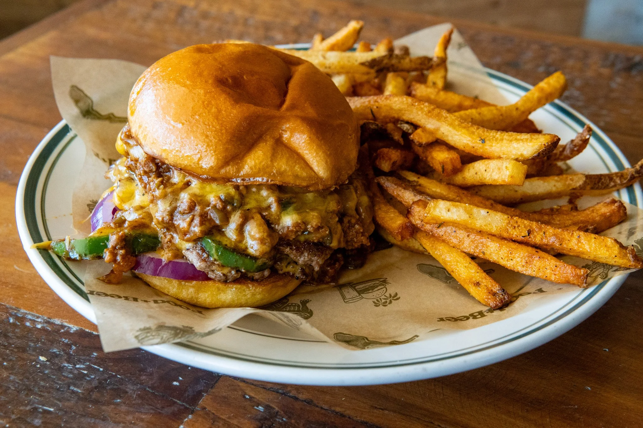 A plate with a cheeseburger topped with a brioche bun and a side of French fries on a wooden table.