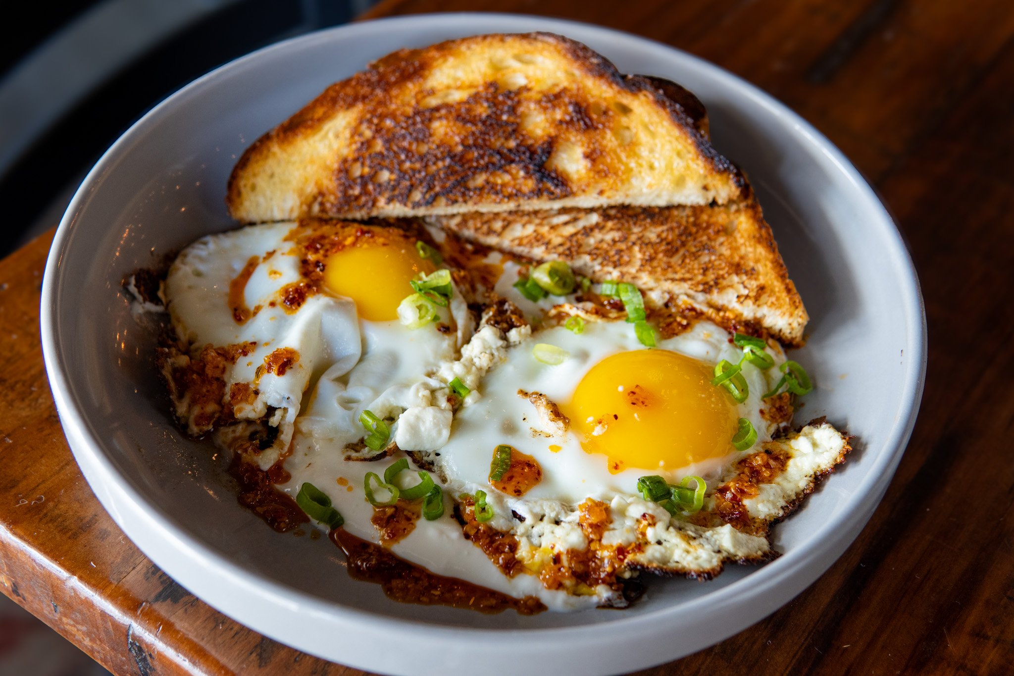 Turkish Eggs - two feta-grilled eggs, garlic yogurt, chili crisp, fresh dill, and sourdough toast.
