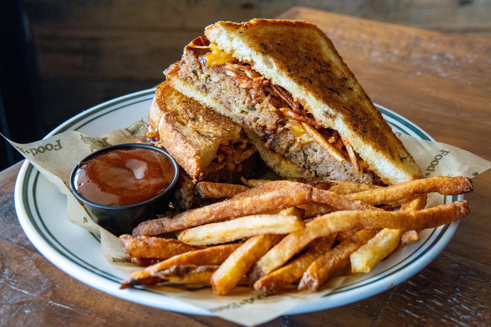 A plate of a cheeseburger with french fries and a side of dipping sauce, sitting on a wooden surface.