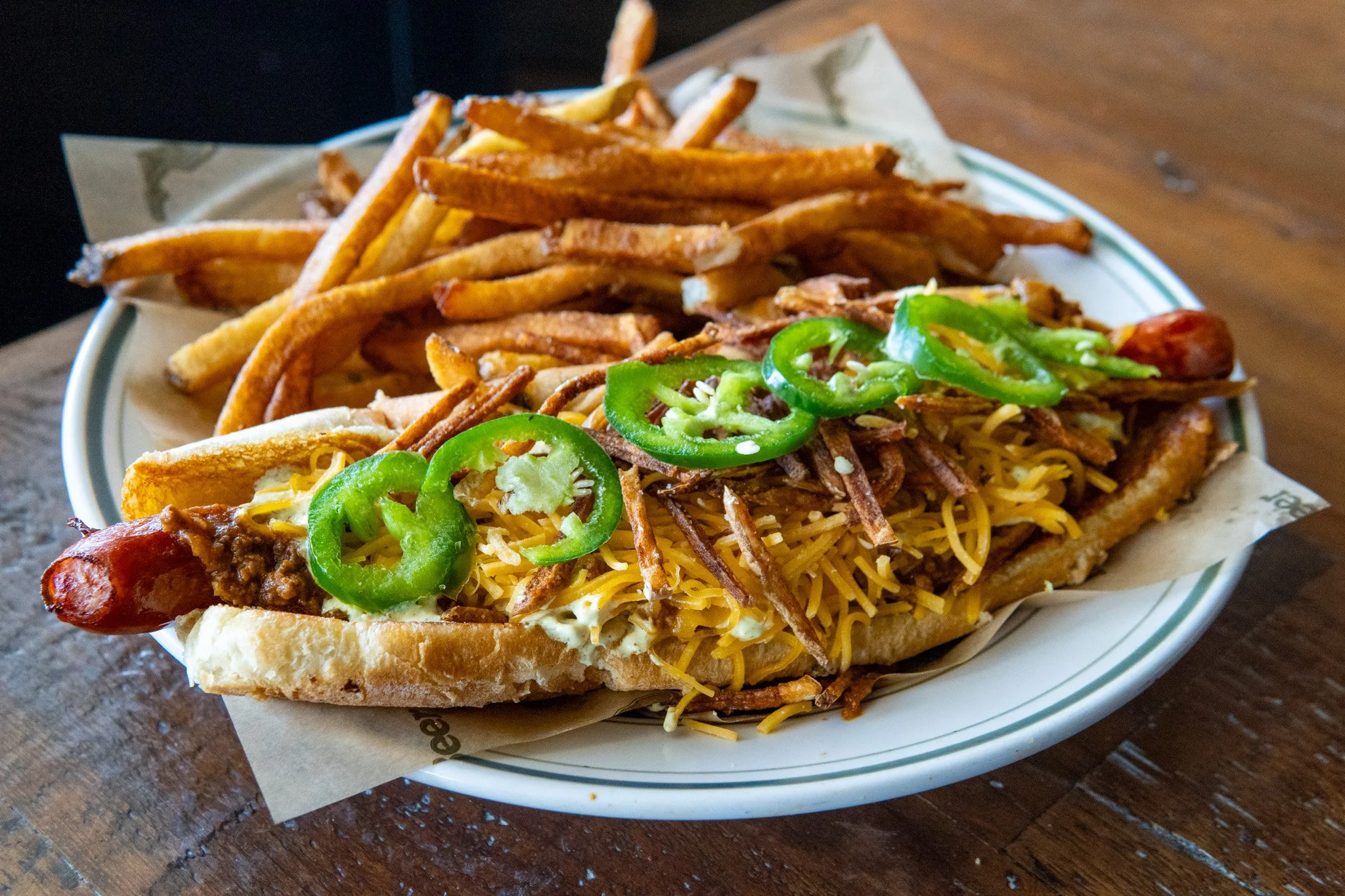A Philadelphia cheesesteak sandwich topped with sliced green peppers, shredded cheese, and crispy fried onions, served on a hoagie roll with French fries on the side.