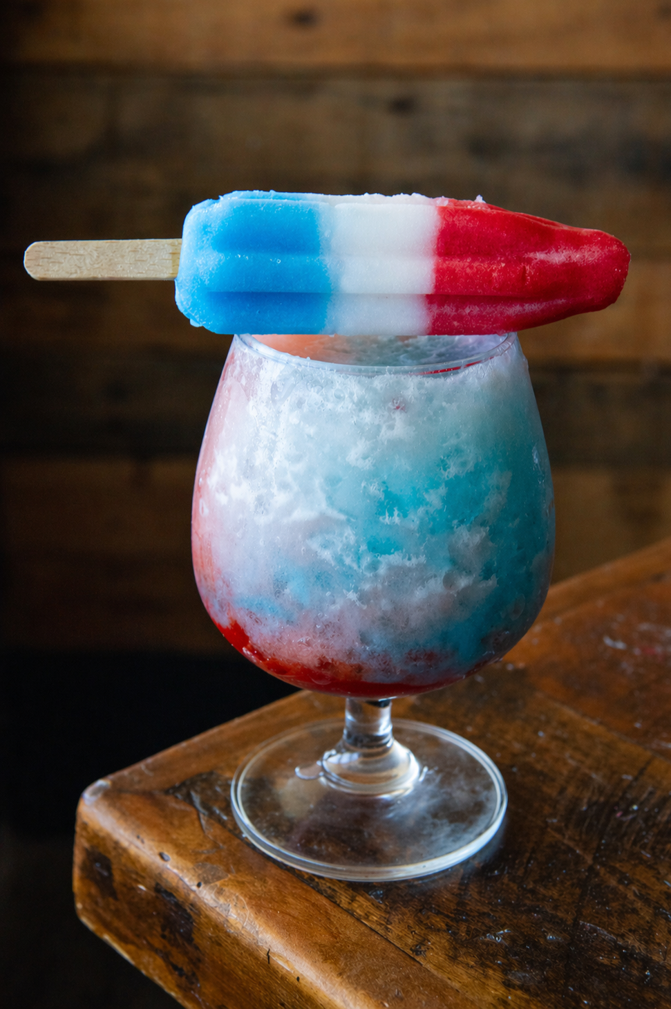 A glass of iceless red, white, and blue frozen drink with a red, white, and blue popsicle on top.