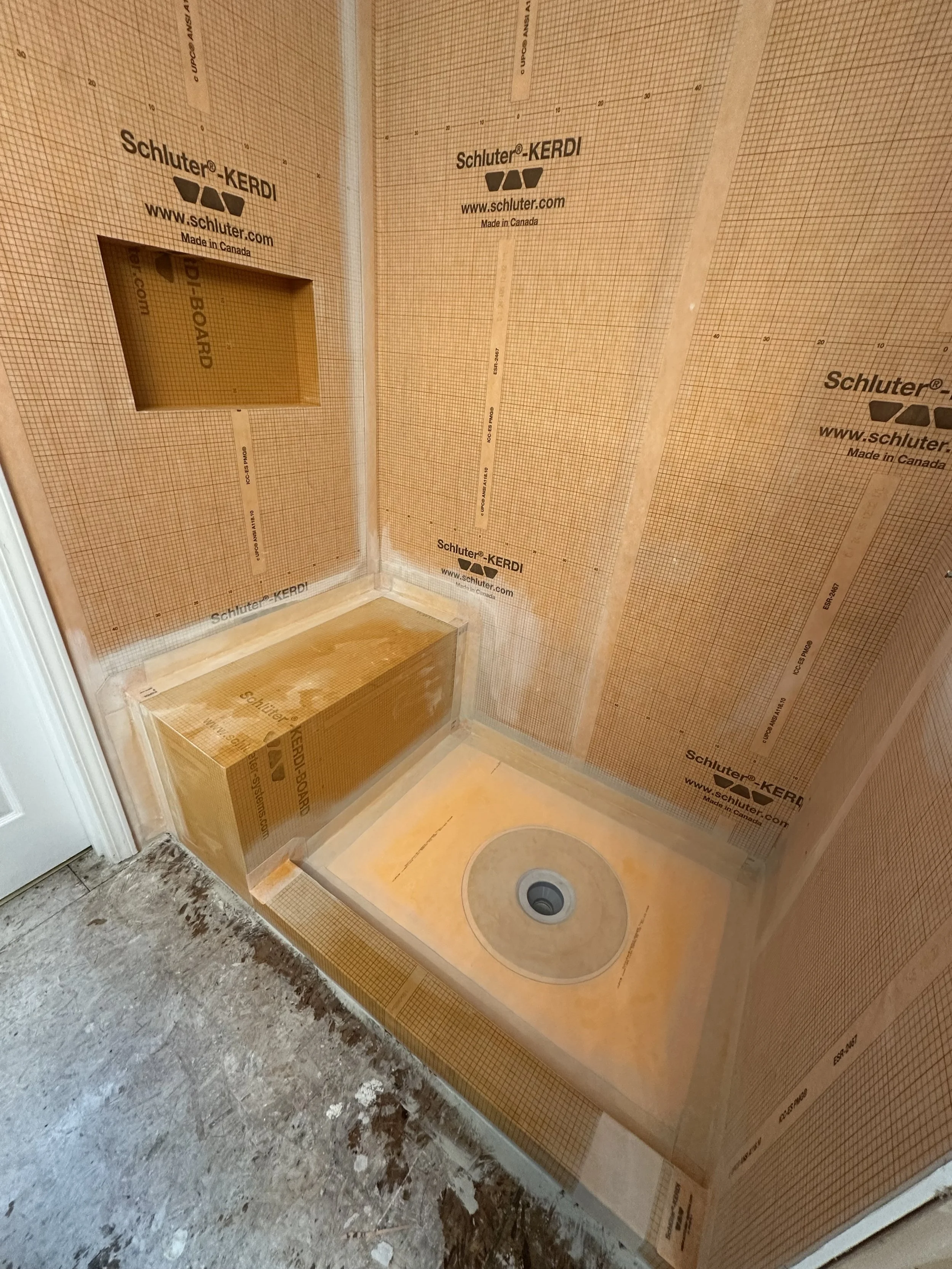 Construction of a shower stall with waterproofing membrane, drywall, and drain installed.