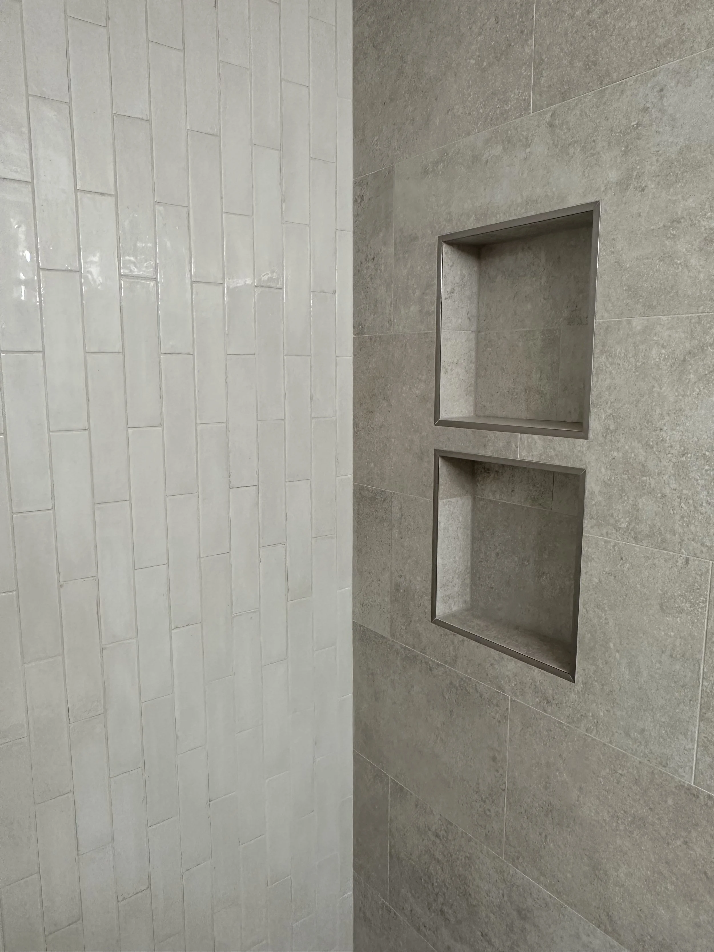 Close-up of a shower wall with two built-in rectangular shelves, one within the other, on a tiled wall with a mix of textured and smooth tiles.