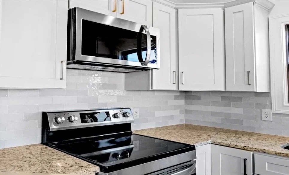 Modern kitchen with white cabinets, granite countertops, a stainless steel microwave, and electric stove.