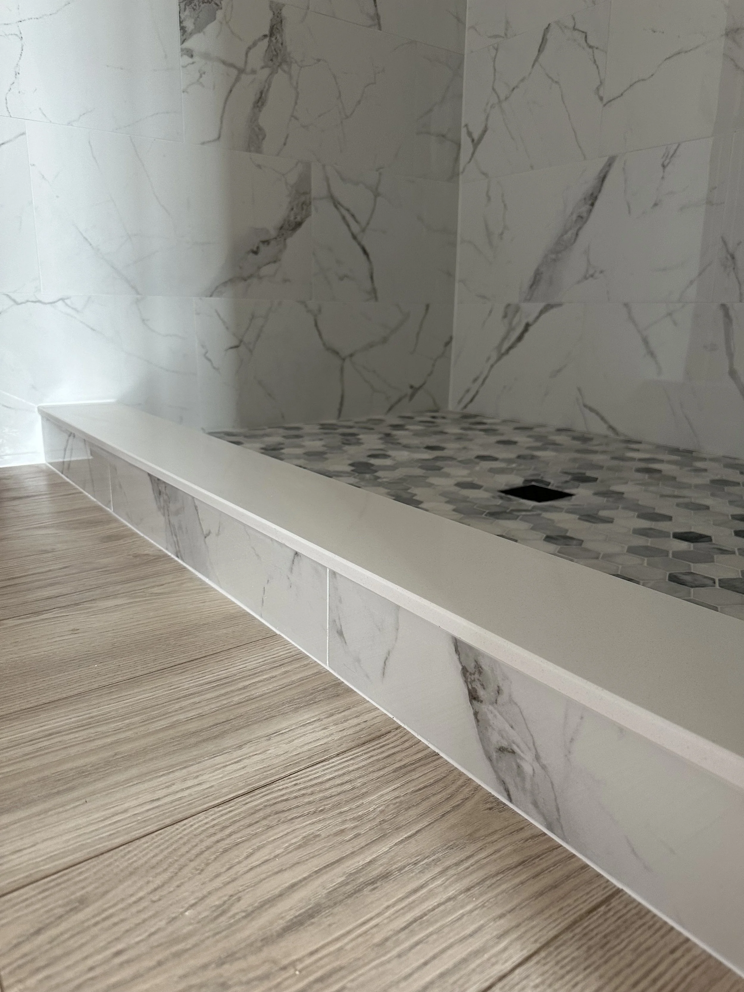 Close-up of a marble shower with a pebble tile floor and wooden flooring outside the shower.