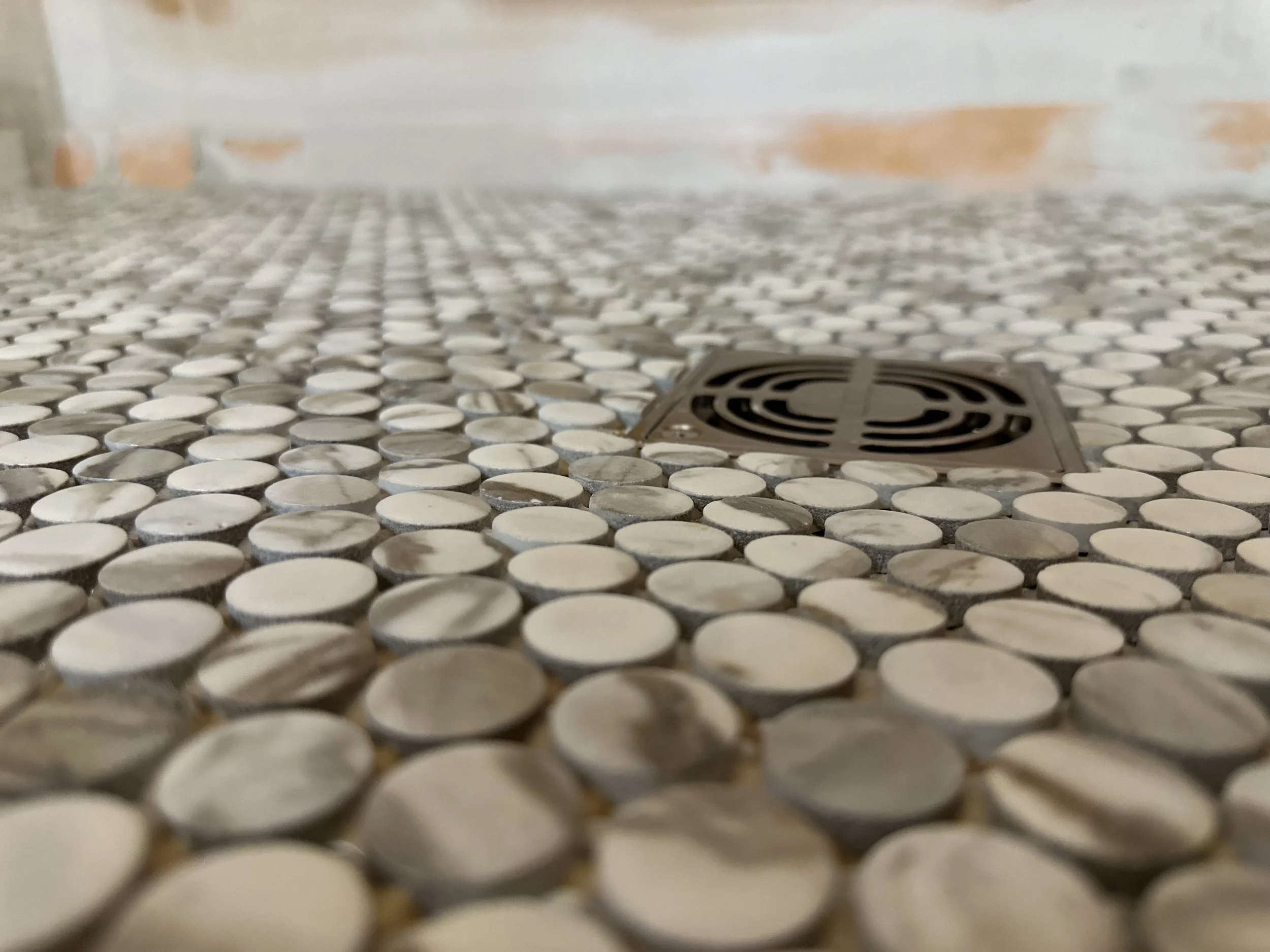 Close-up view of a tiled floor with round mosaic tiles and a floor drain.