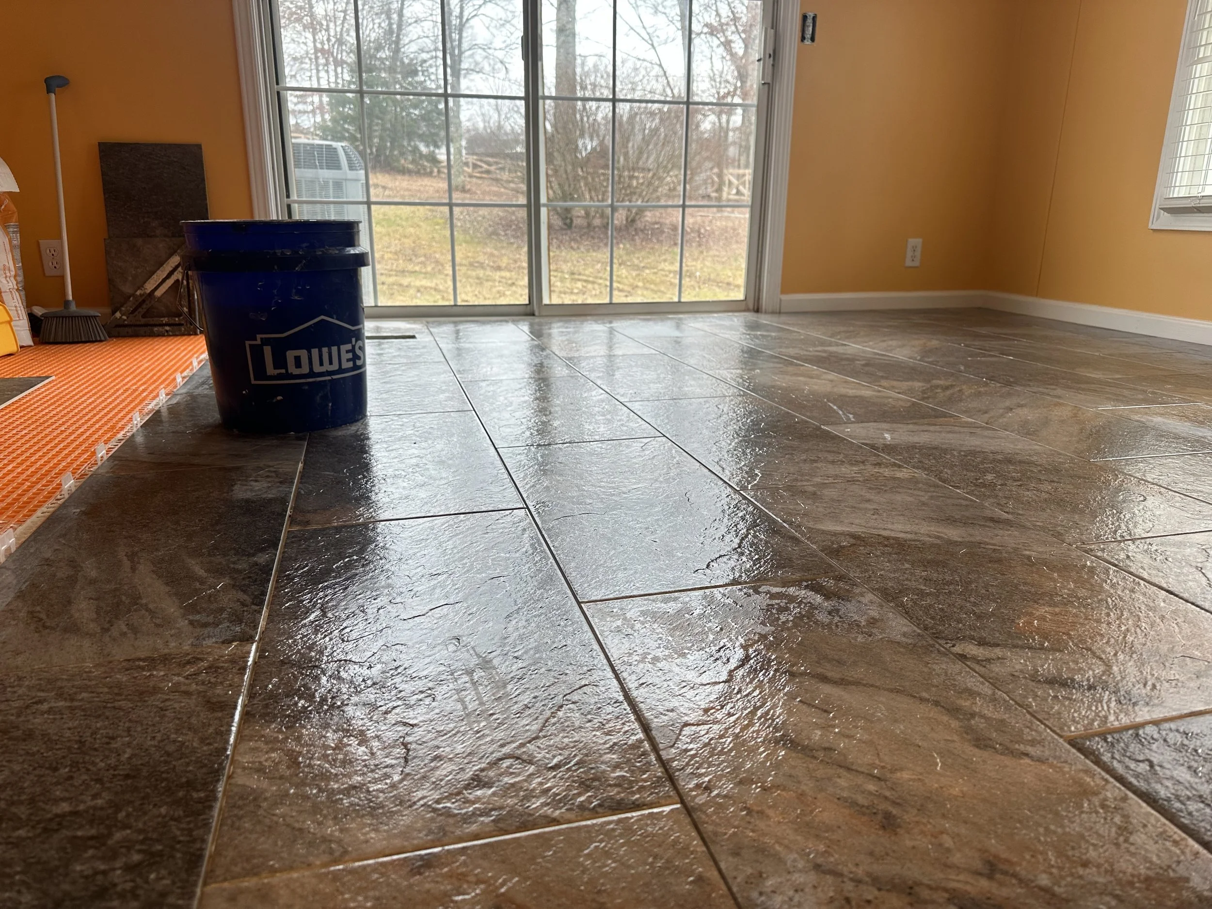 A newly installed tiled floor inside a room with yellow walls and large sliding glass doors leading outside.