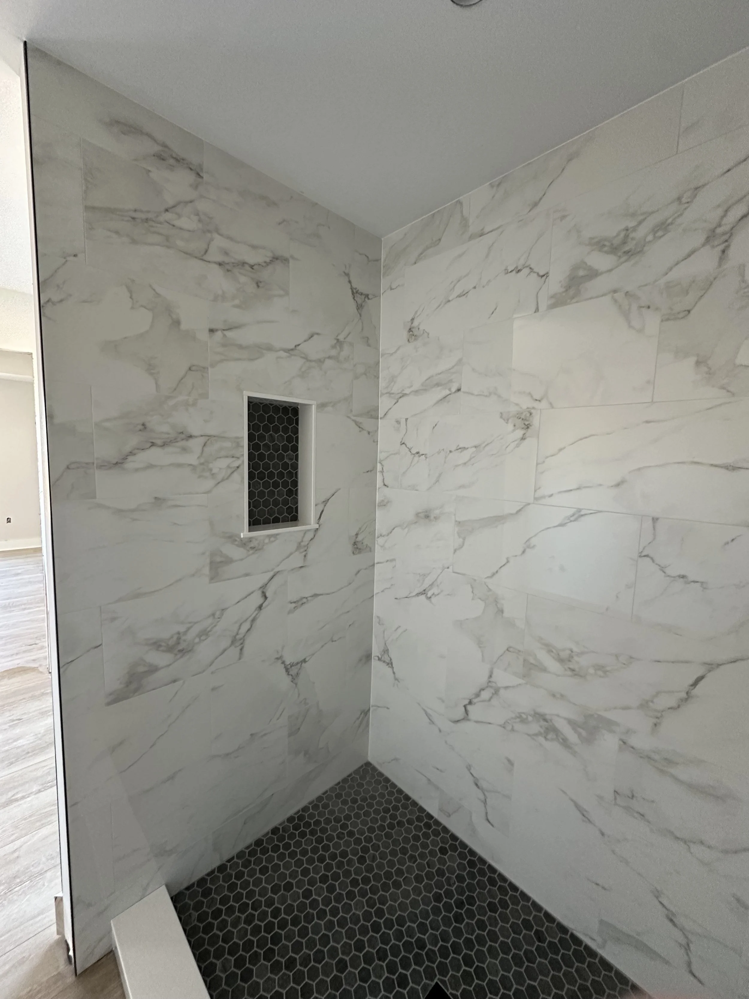 A marble-tiled shower with a small built-in shower niche and a dark hexagonal tile floor.
