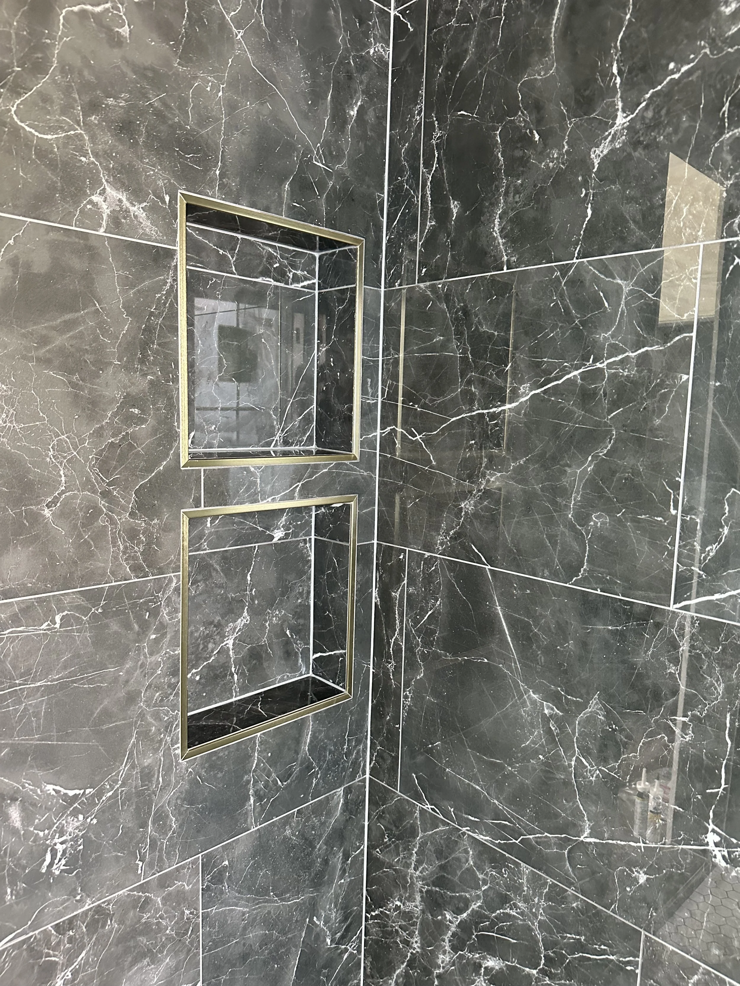 Close-up of a black marble shower wall with two square built-in shelves outlined in gold.