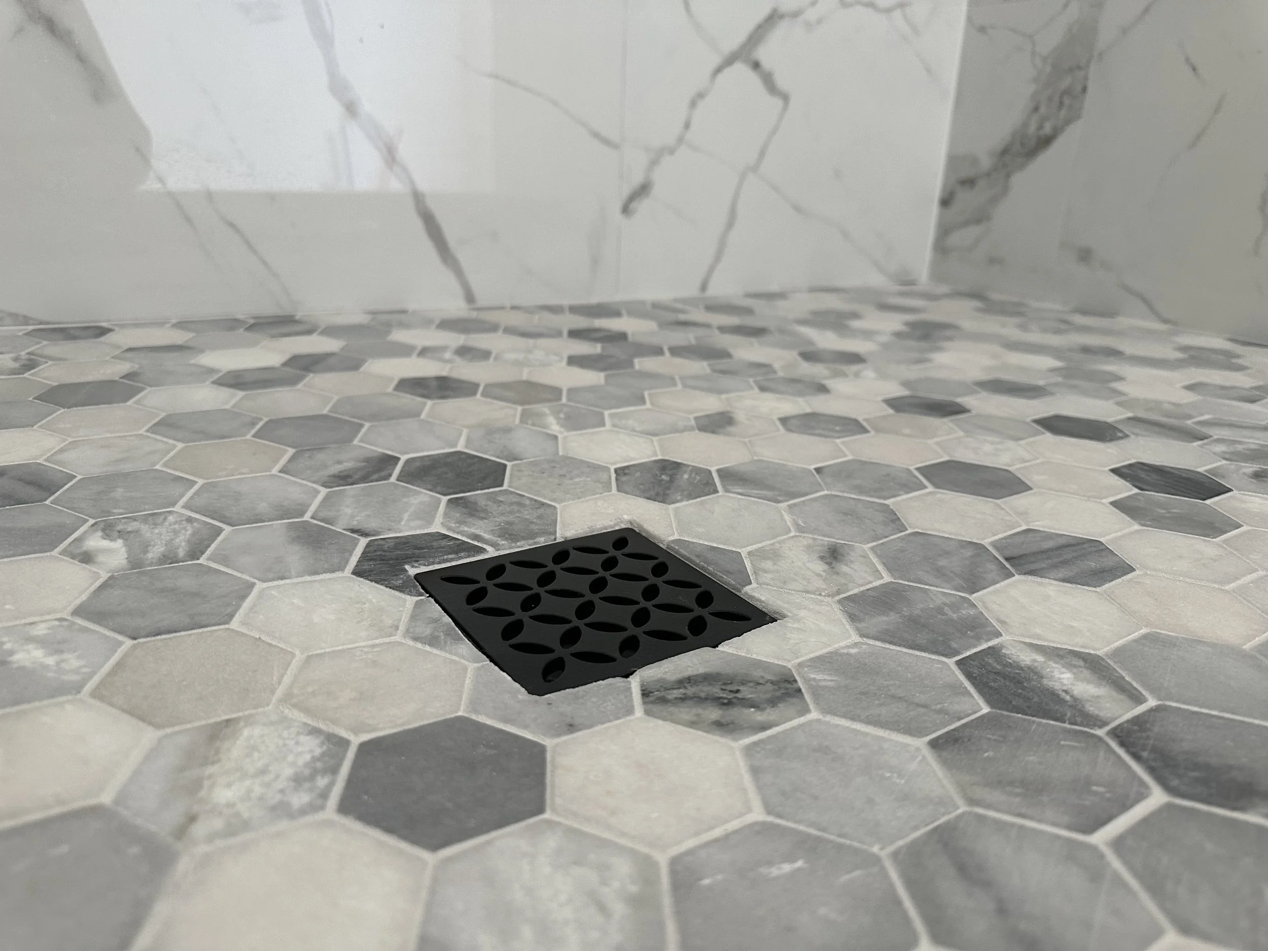 Close-up view of a marble and hexagon tile shower floor with a black square drain.