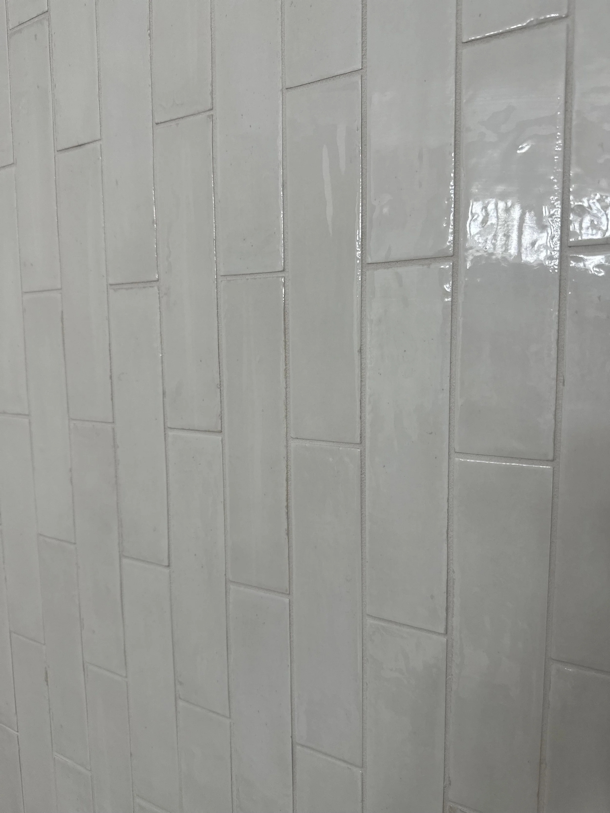 Close-up image of a tiled wall with glossy, rectangular white tiles arranged in a horizontal pattern.