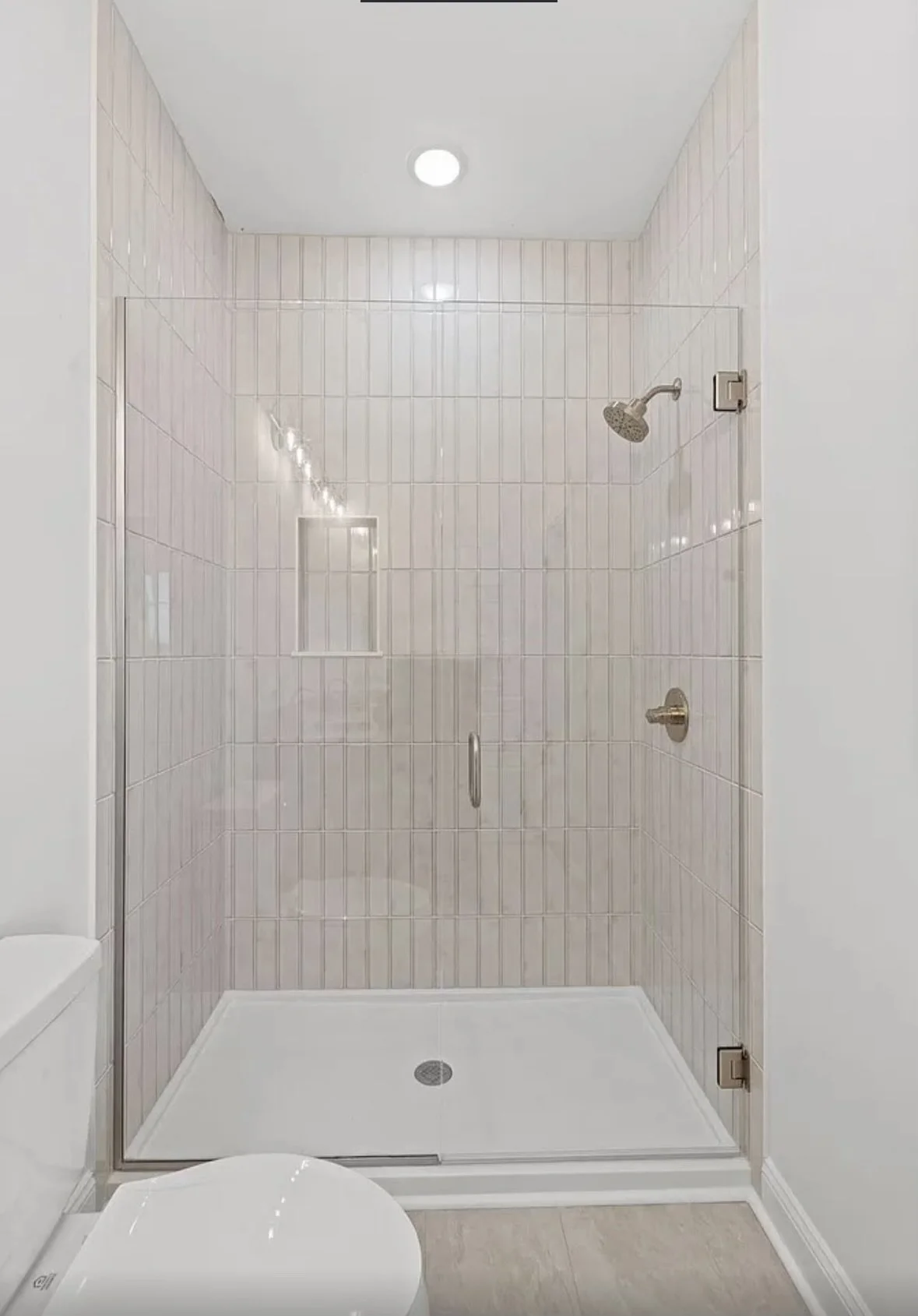A shower with a glass door, beige tiled walls, silver fixtures, and a recessed ceiling light.